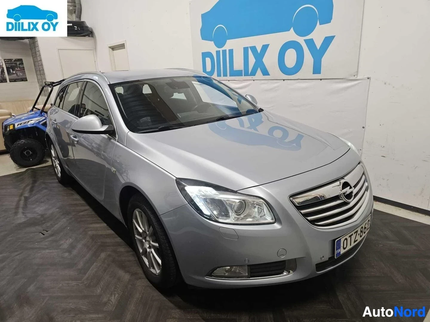 Etuviisto, nokka oikealle: Hopeanvärinen Opel Insignia -farmari sisätiloissa kylmävarastossa, kuvattu vasemmalta etupuolelta, naamio ja etusäleikkö näkyvissä.