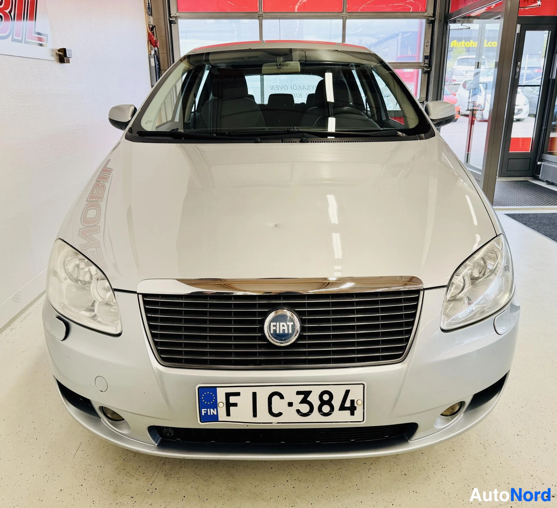 Edestä: Valkoinen Fiat Croma edestä kuvattuna sisätiloissa. Näkyy etulasit, etupäähän, Fiat-merkki ja rekisterikyltti
