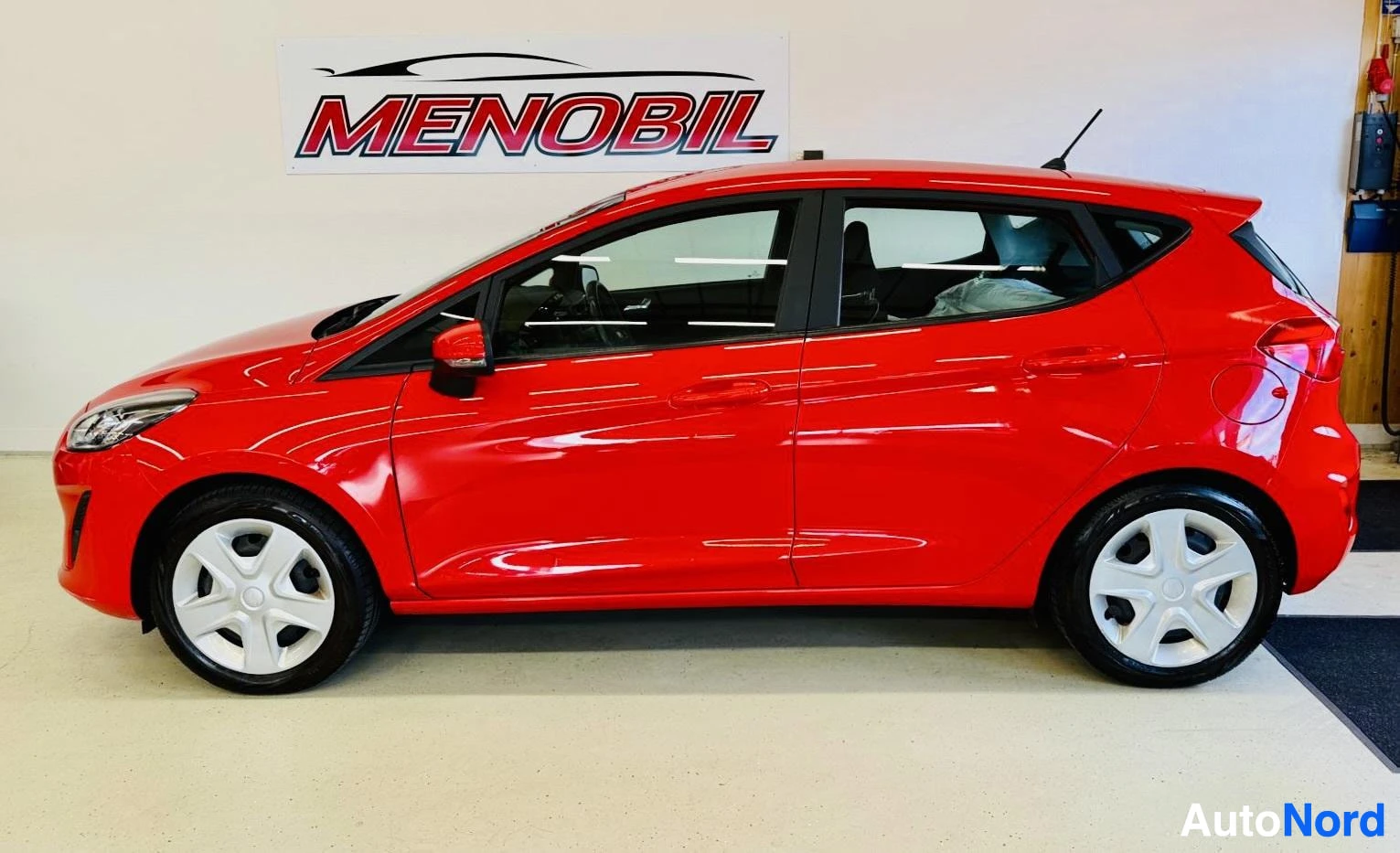 Sivulta: Punainen Ford Fiesta sivuprofiilissa, katsottuna vasemmalta puolelta varastotiloissa.
