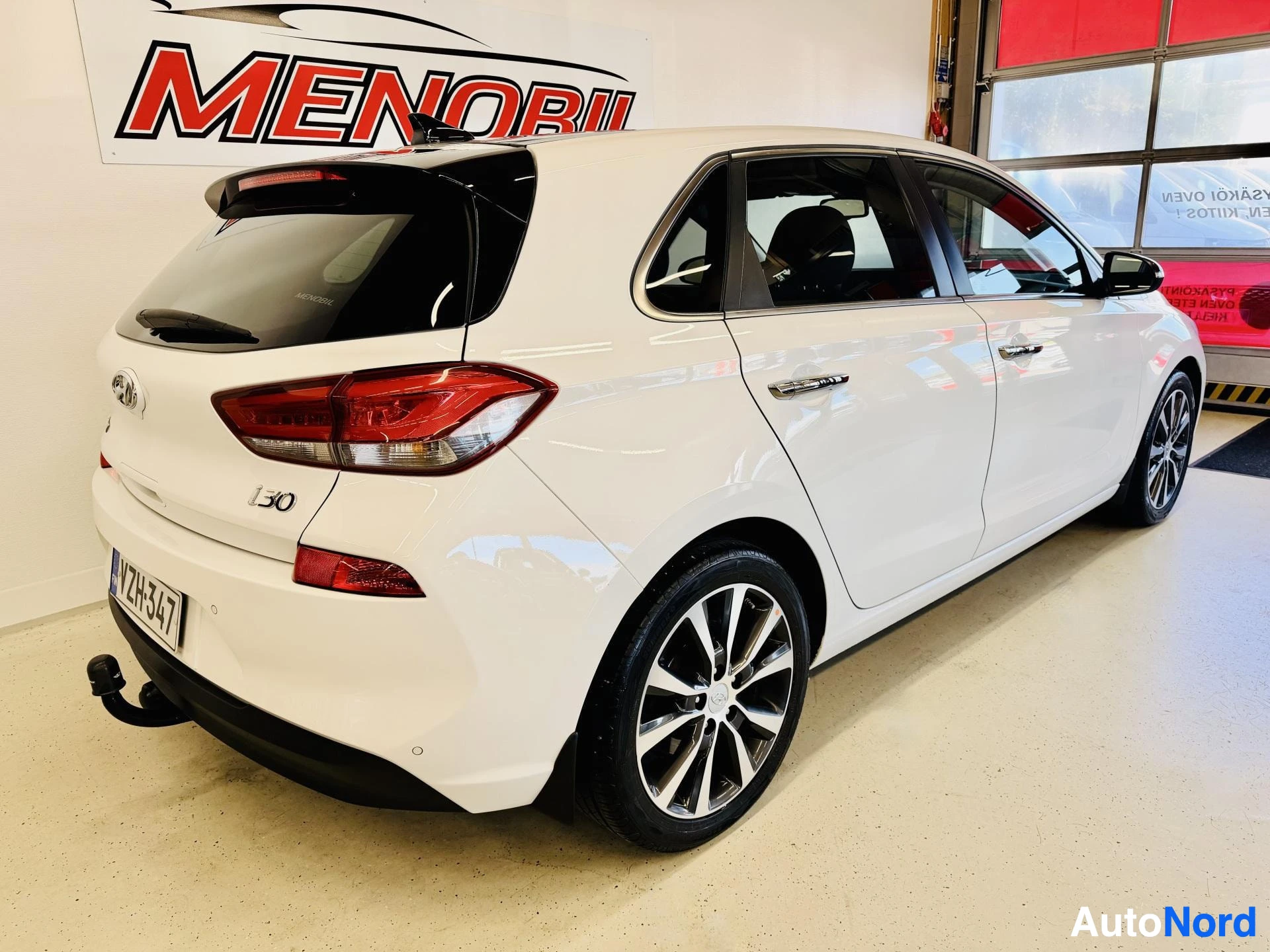 Takaviisto: Valkoinen Hyundai i30 kolmiveto takaapäin, takahatch auki, näkyy rekisterinumero ja vetokoukku