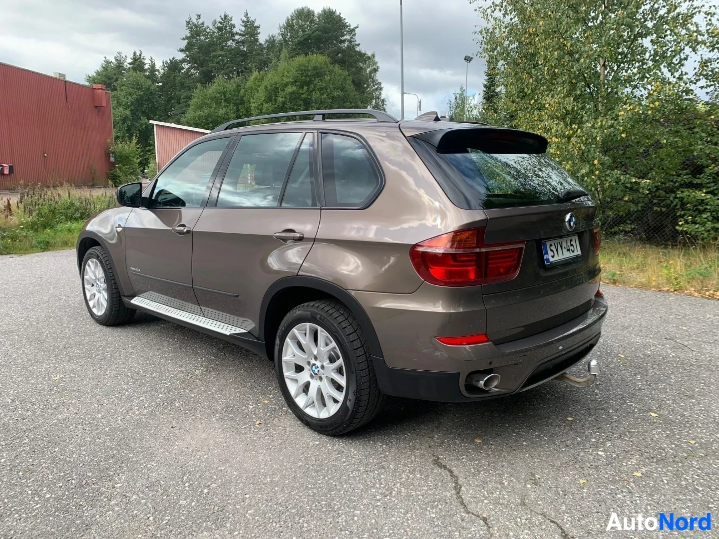 Takaviisto: Ruskea BMW X5 -maastoauto takaviistosta oikealle, parkkipaikalla teollisuusrakennusten edessä