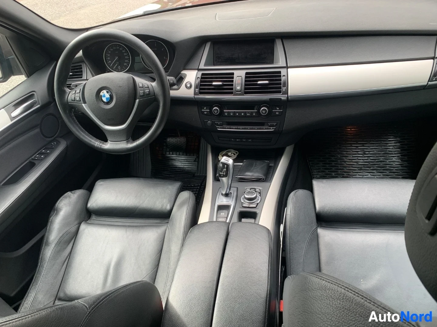 Ohjaamo: Auton sisustus etupuolelta kuvattuna. Näkyvät ohjauspyörä BMW-logolla, neljä nahkaa pinnoitettua istuinta, ilmastointi- ja äänentoistolaitteet, sekä keskikonsoo