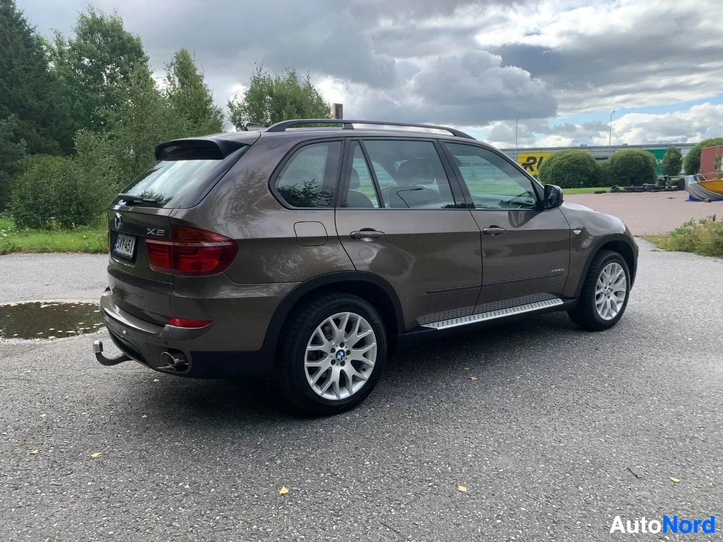 Takaviisto: Ruskea BMW X5 -maasturi kuvattuna takaa vasemmalta kolmen neljänneksen kulmasta, pysäköitynä asfalttitiellä.