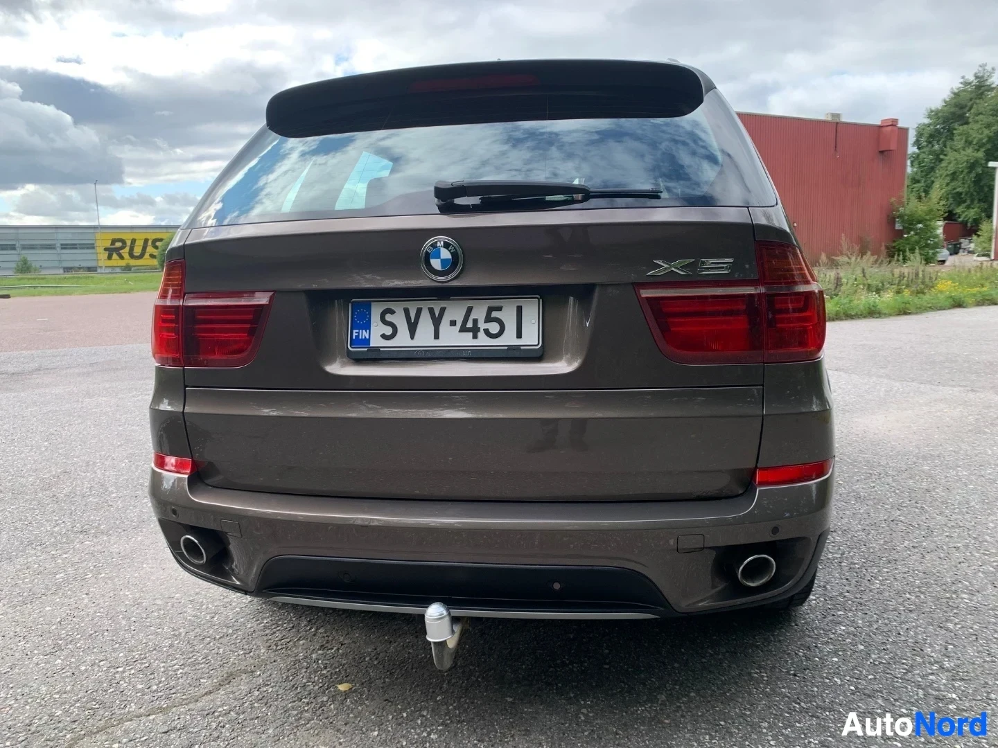 Takaa: BMW X5:n taka näkymä harmaassa värityssä, rekisterikilvellä, punaiset takalampyt, mustalla takasiivellä BMW-logo ja X5-merkintä, vetokoukku asennettu