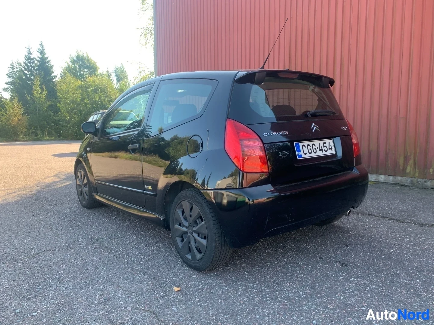 Takaviisto: Musta Citroën C2 takapuoli kolmen neljänneksen näkymässä, rekisteritunnus CG6454, pysäköity betonille punaiselle metallivaraston edessä