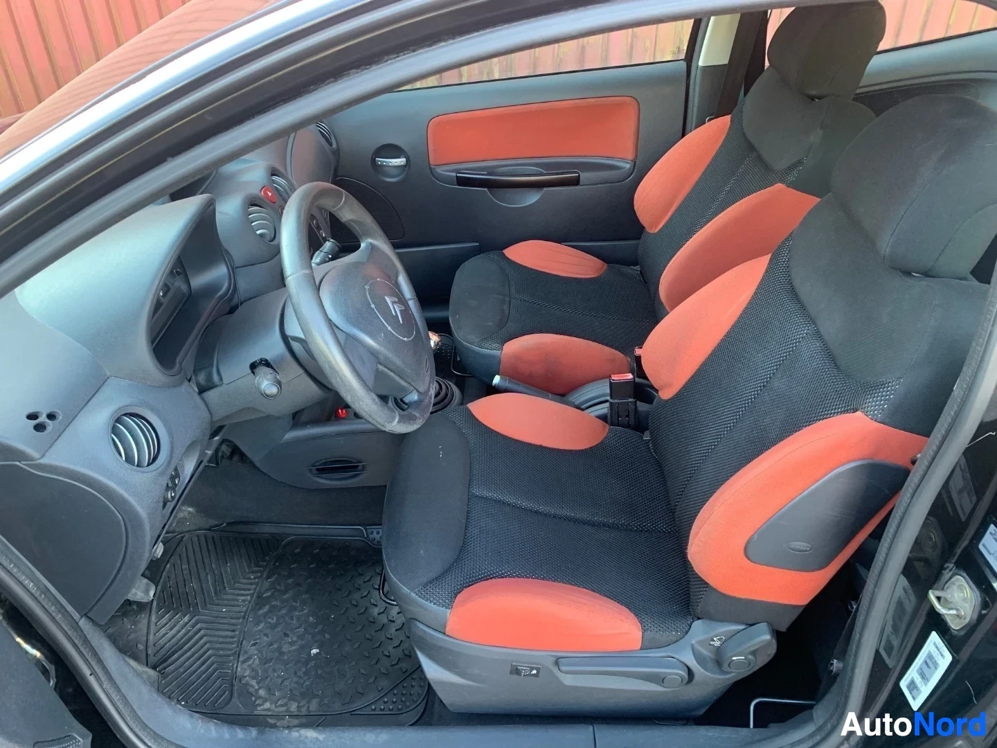 Etuistuimet: Citroën C2 sisusta etuosasta, mustat ja oranssit istuin, mustat matot, valkea ohjauspyörä.
