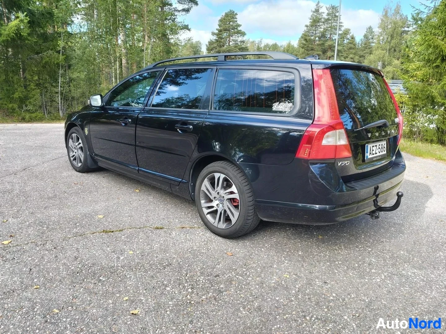 Takaviisto: Musta Volvo V70 -monivaunuauto kuvattuna kolmen neljänneksen kulmasta takaaa, oikealta puolelta. Takaovi on avoinna. Punaiset takavalaisimet, V70-merkintä näkyy