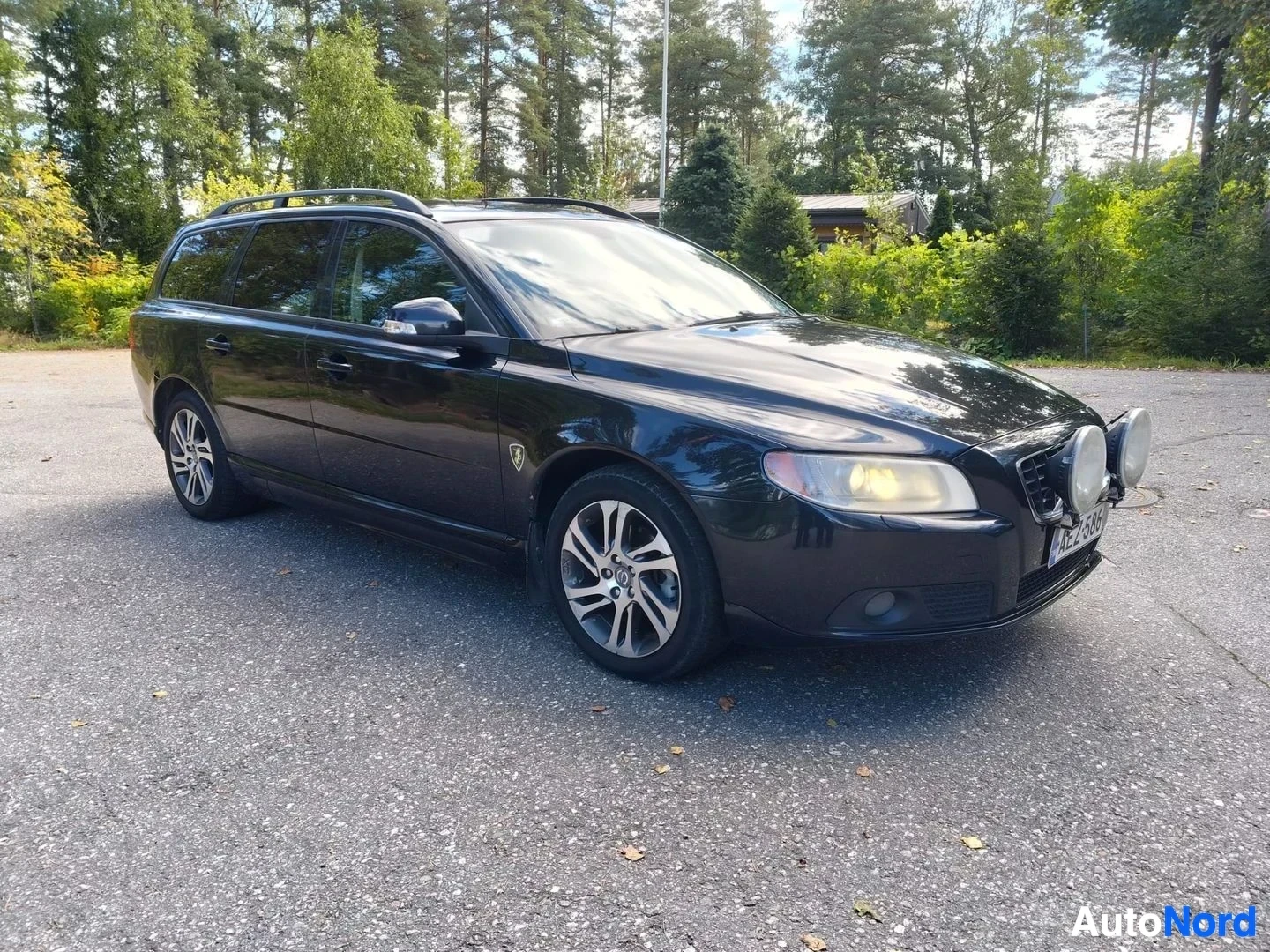Etuviisto, nokka vasemmalle: Musta Volvo V70 estate, etupuolen kolmen neljänneksen kuva, kuljettajan puoli kohti. Xenon-ajovalot näkyvät keltaisella/kiilaavalla valolla. Hopeanväri