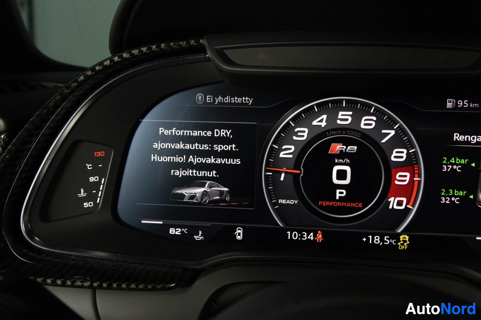 Yksityiskohta: Audi R8:n instrumenttipaneeli, jossa näkyvät mittarit, infotainment-näyttö, joissa on performance-ajotilan tiedot, ja ratti.