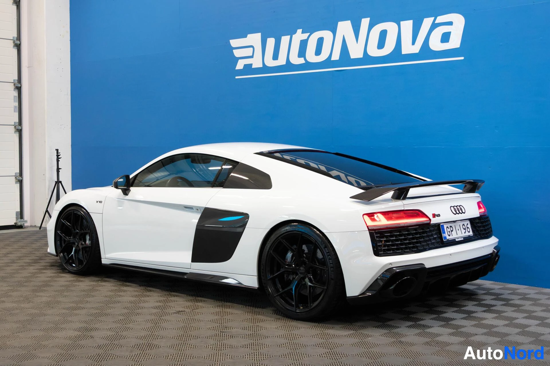 Takaviisto: Valkoinen Audi R8 V10 sivusta kauempaa, näkymä oikealta puolelta ja takaosasta, mustat alloy-vanteet, AutoNova-tausta