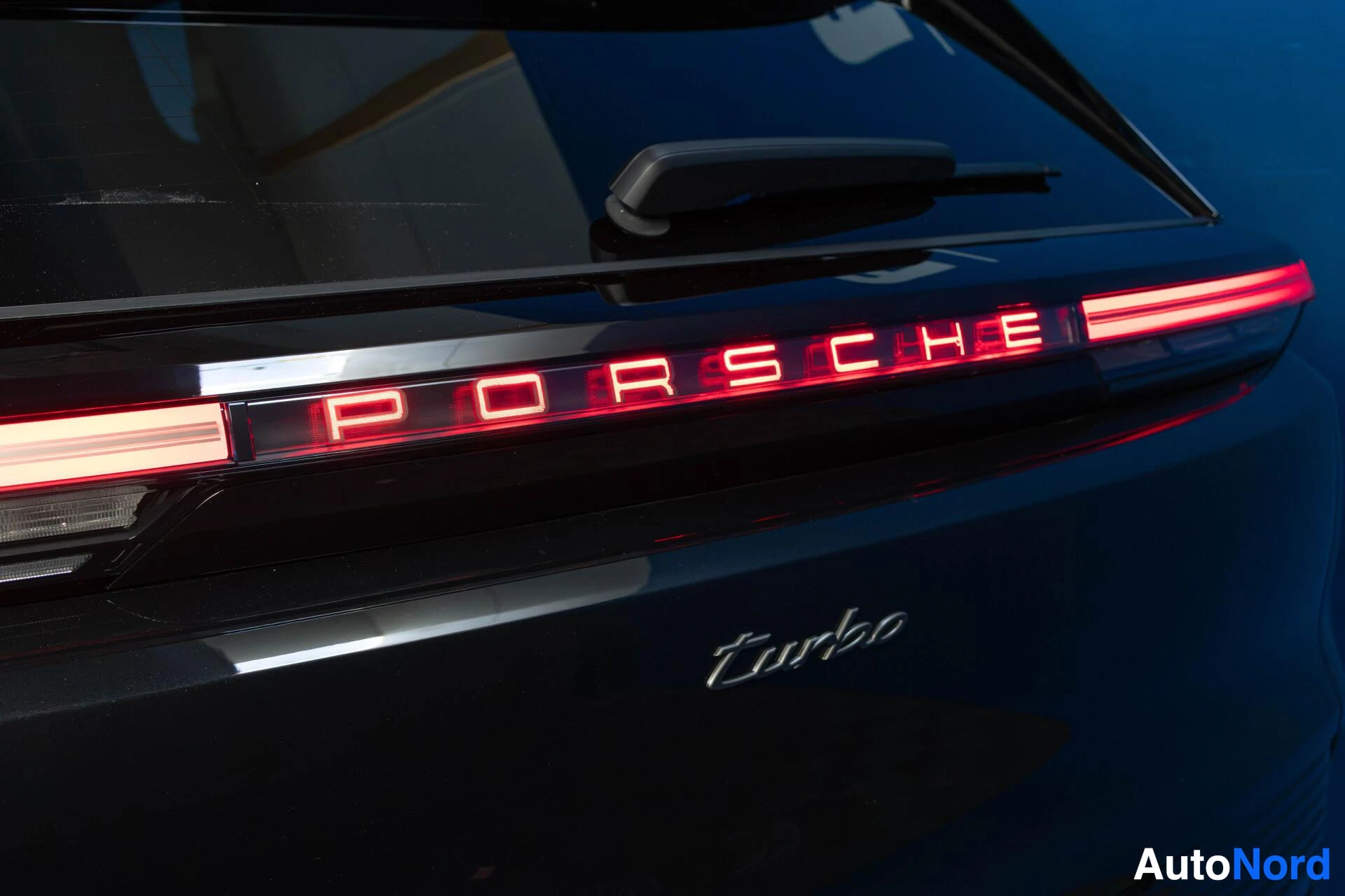 Yksityiskohta: Mustan auton takaosa lähikuvassa. Takavalot ovat päällä ja niissä lukee "PORSCHE" punaisilla kirjaimilla. Tavaratilan luukussa on "Turbo"-merkki.