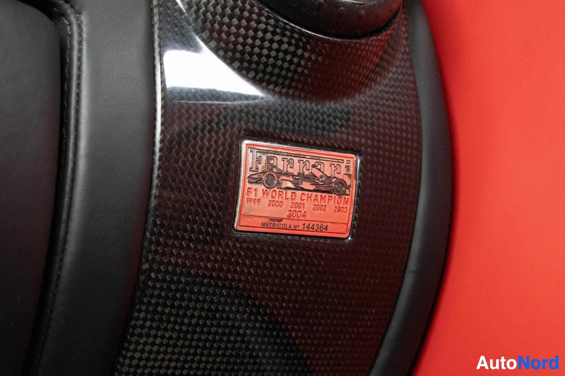 Yksityiskohta: Metallinen laatta, jossa lukee "Ferrari F1 WORLD CHAMPION" ja vuosilukuja 1999-2004 sekä "MATRICOLA N° 144364".