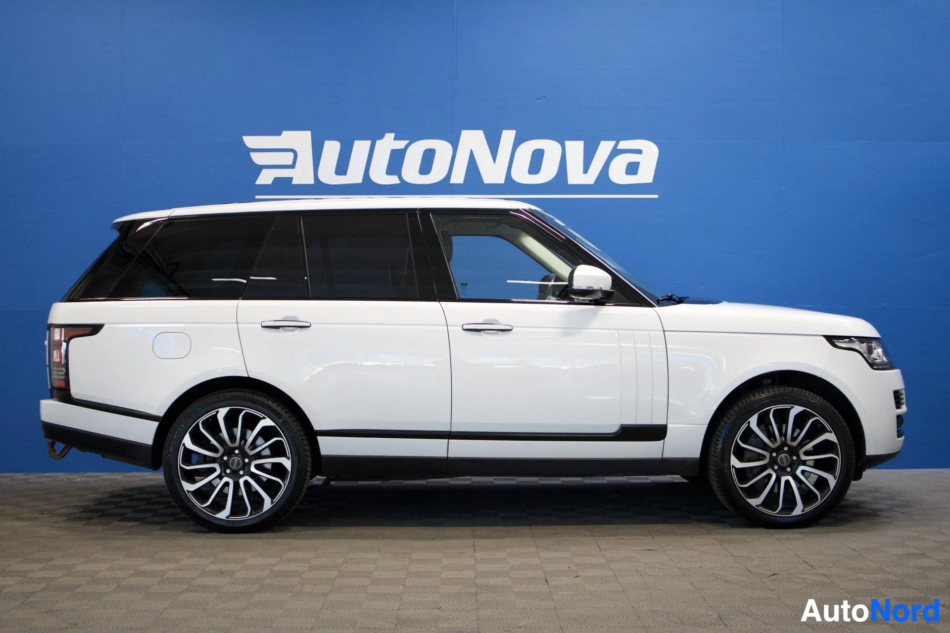Sivulta: Valkoinen Land Rover Range Roverin oikea kylki. Autossa on kaksiväriset vanteet ja tummennetut takalasit. Taustalla on sininen seinä, jossa lukee "AutoNova".