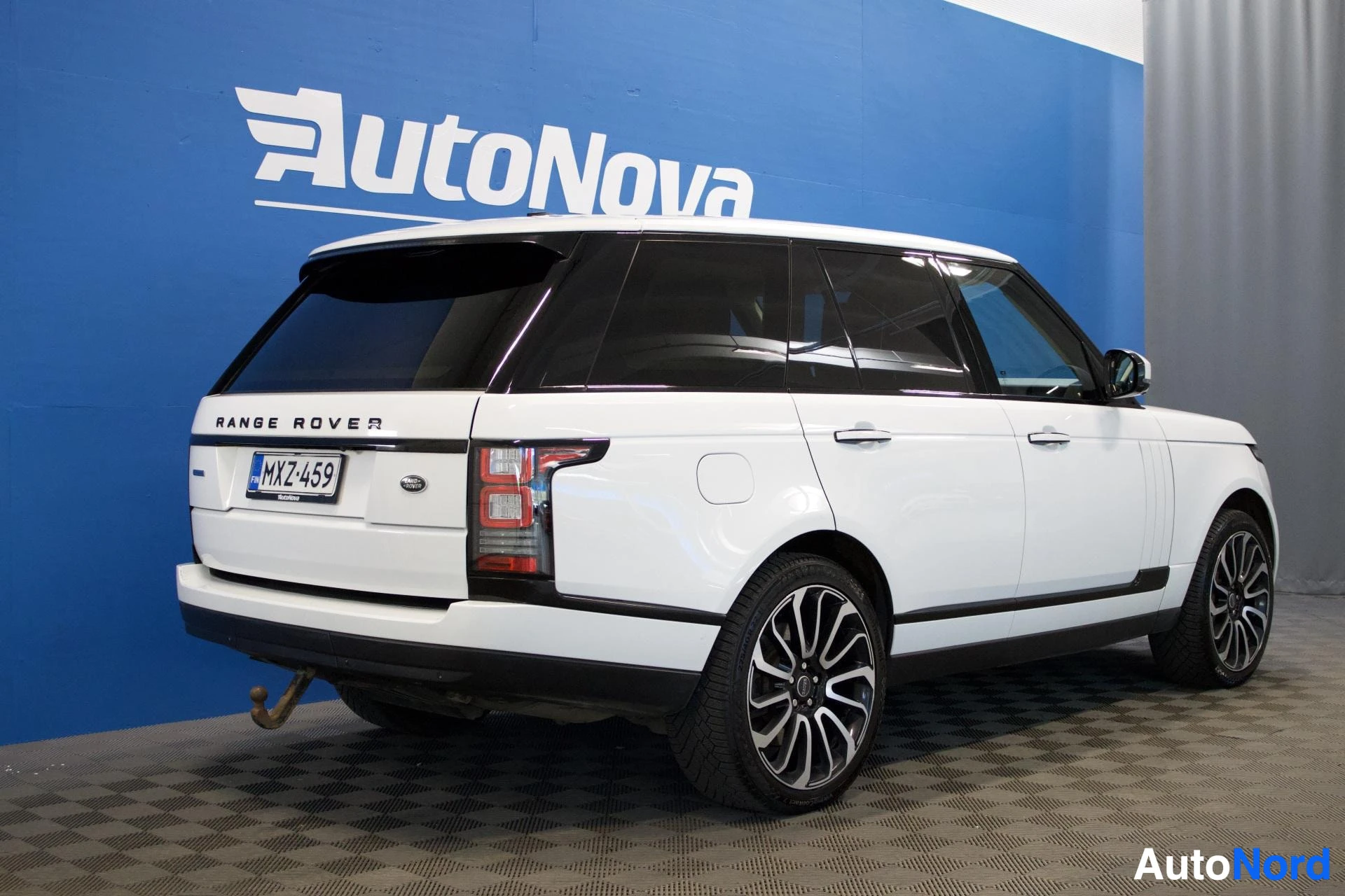 Takaviisto: Valkoinen Land Rover Range Roverin takaa oikealta kuvattu. Autossa on vetokoukku, tummennetut takalasit ja kaksiväriset vanteet. Rekisterikilpi on. Taus