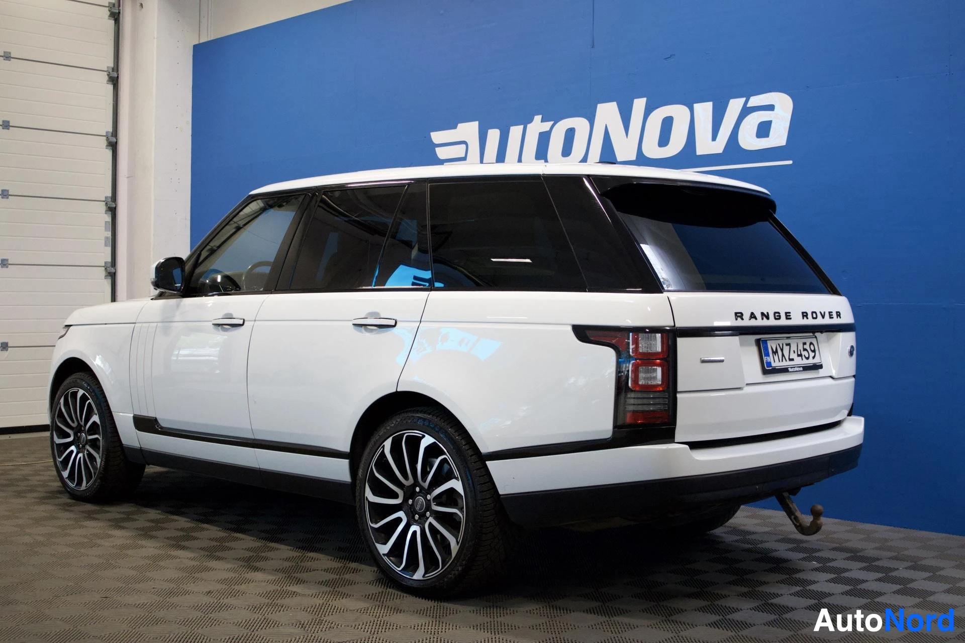 Takaviisto: Valkoinen Land Rover Range Roverin takaa oikealta kuvattu. Autossa on vetokoukku, tummennetut takalasit ja kaksiväriset vanteet. Rekisterikilpi on. Taus