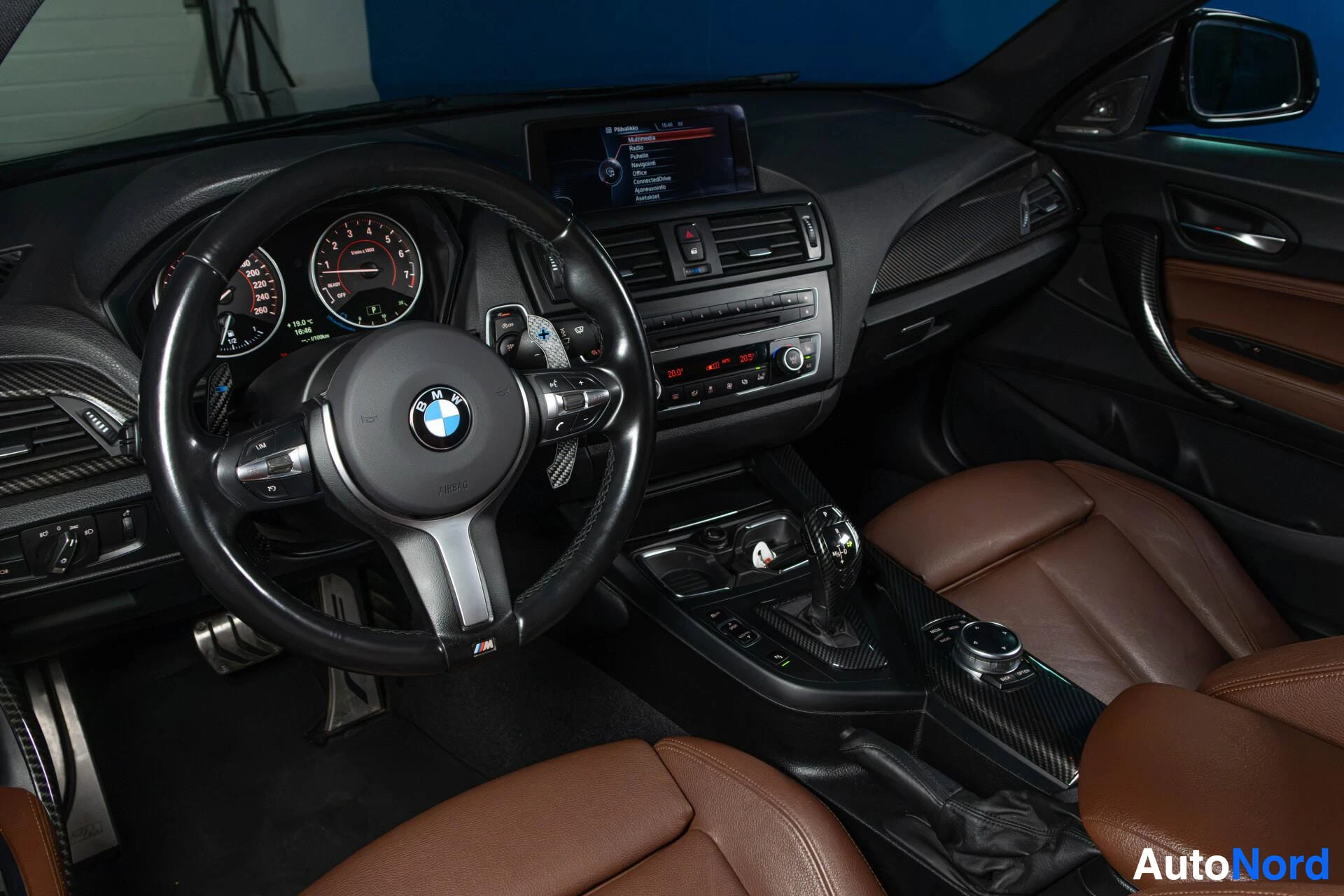 Etuistuimet: Kuljettajan paikka näkymä oikealla BMW-ohjauspyörä, kojelautanäyttö, mustaa ja ruskeaa sisustusta, ruskeat nahkaisten istuinten osat näkyvät.