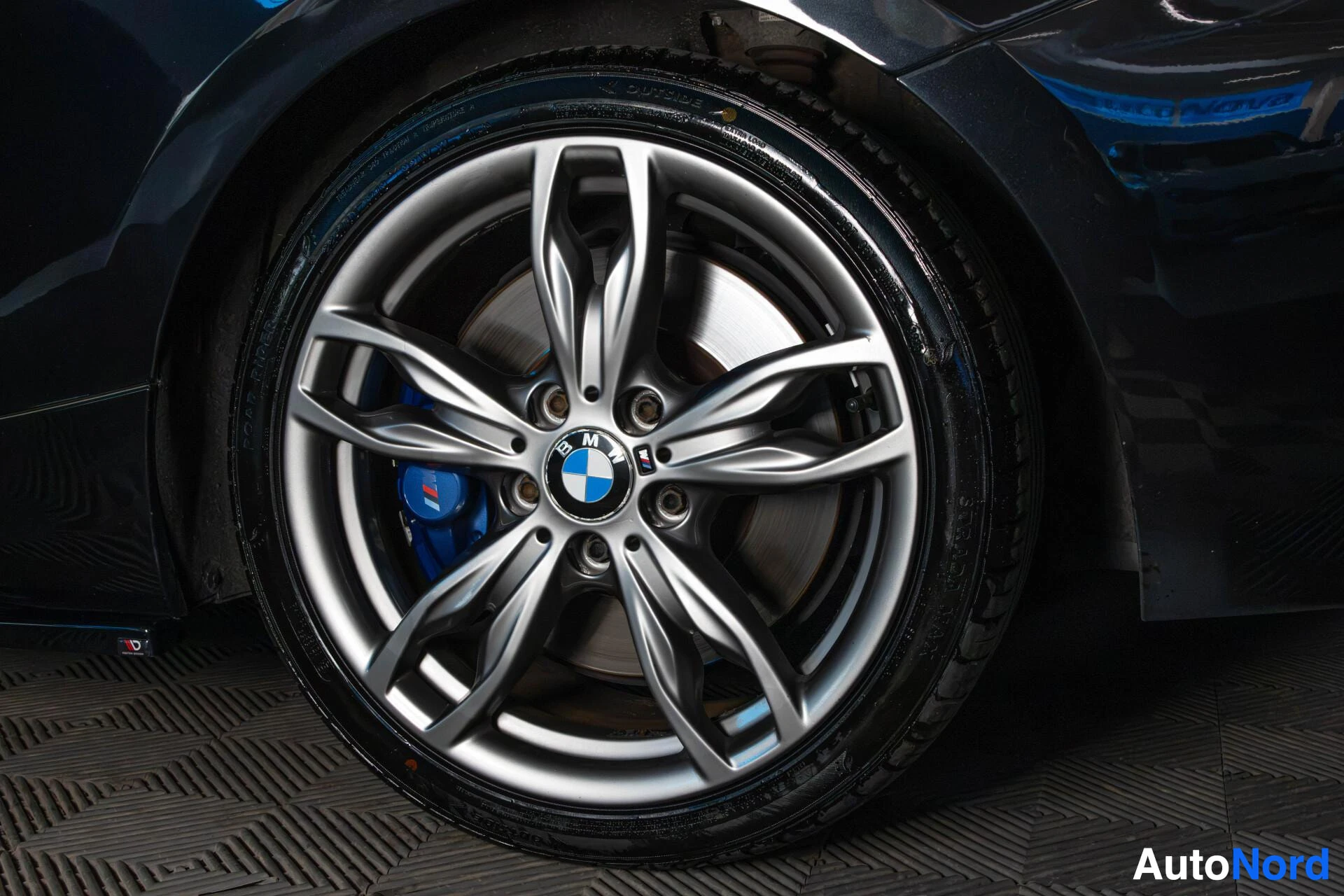 Yksityiskohta: Lähikuva alumiinivanteesta ja renkaasta, jossa näkyy BMW-logo keskellä ja siniset jarrupalat.