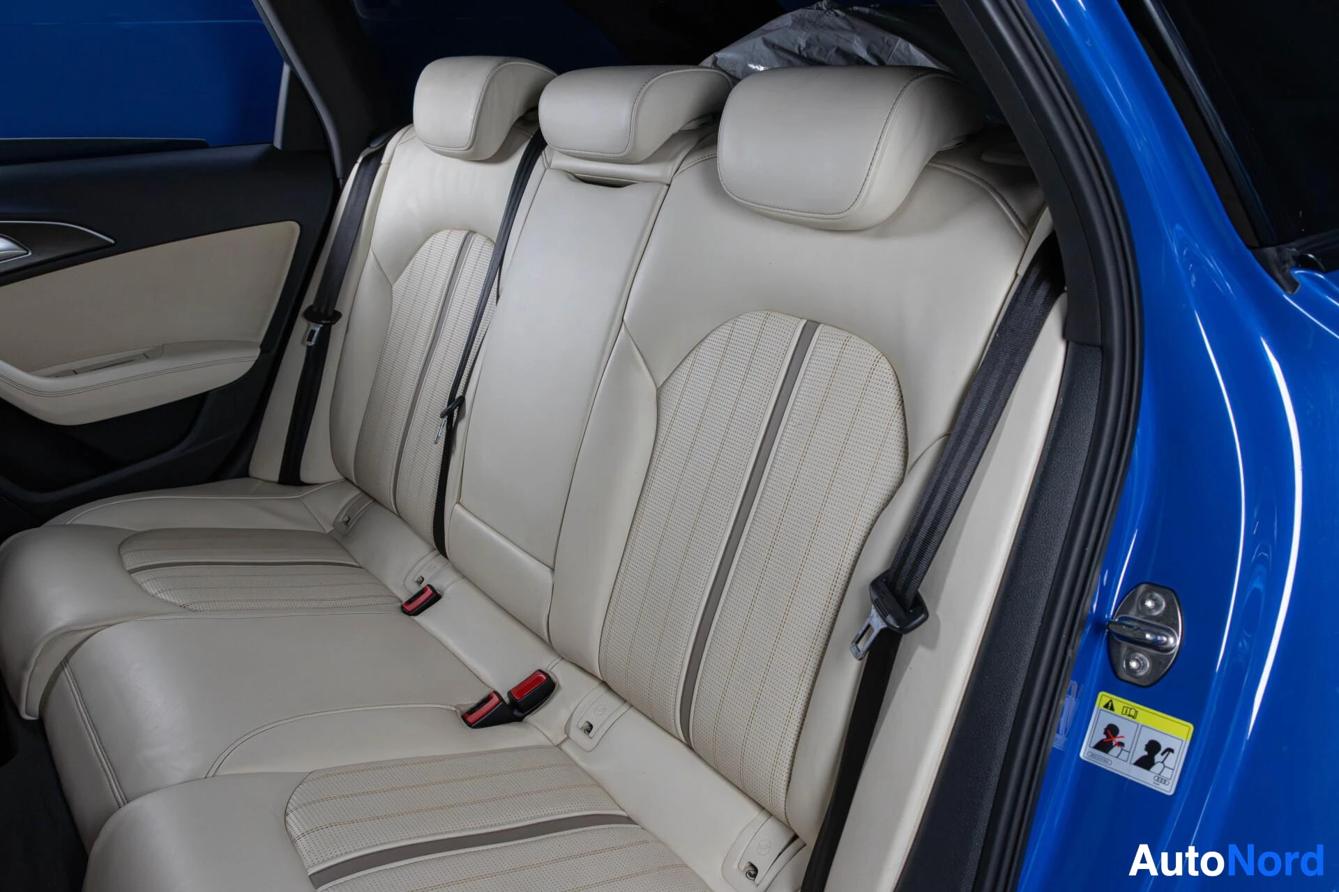 Takaistuimet: Kuva auton takaistuimista. Kolme valkoista tai vaaleaa nahkaverhoiltua istuinta on näkyvissä, kaikissa niskatuet ja turvavyöt. Oikeanpuoleisessa istuimessa on I