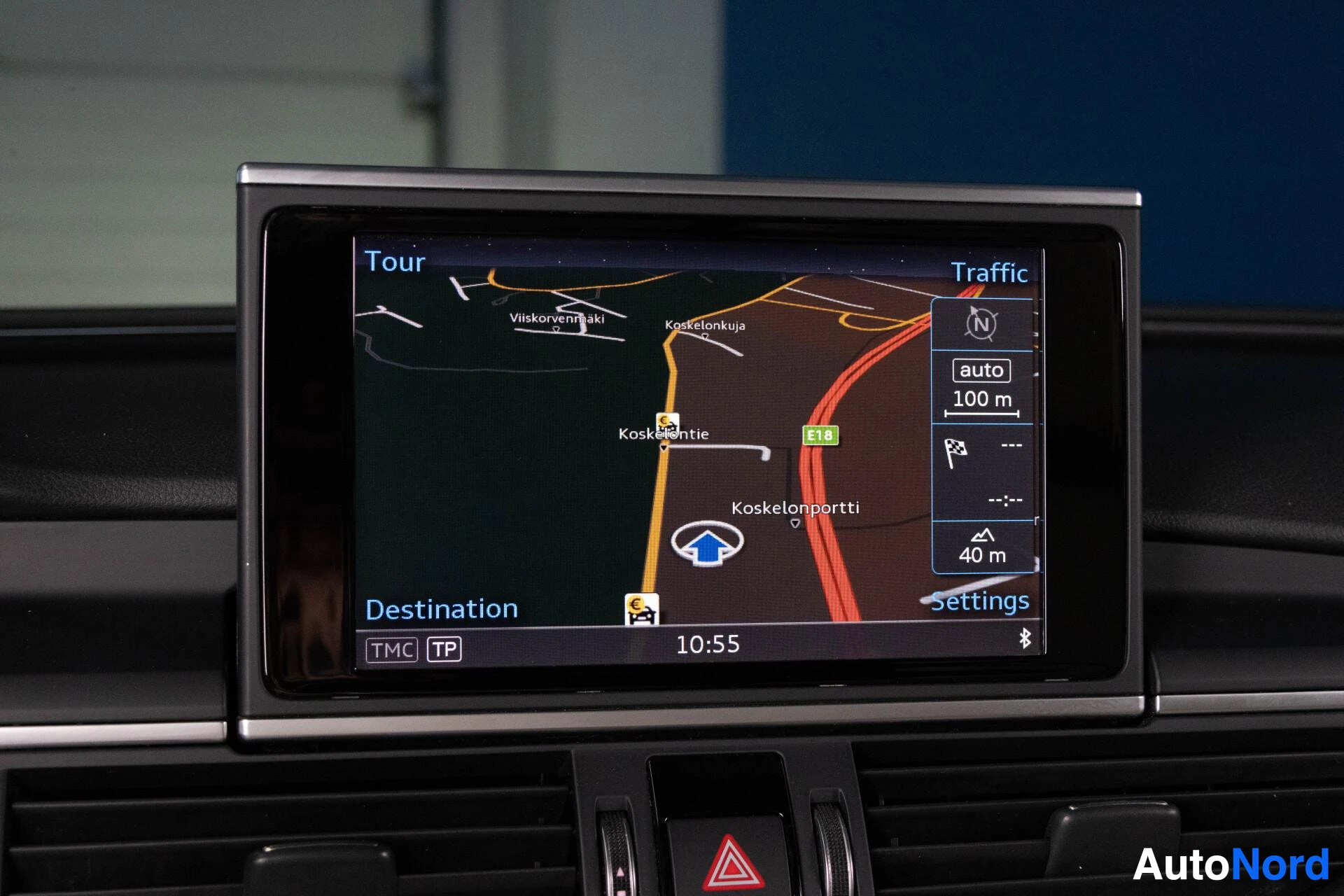 Ohjaamo: Kuva auton infotainment-näytöstä, jossa näkyy navigaatiojärjestelmän kartta. Ruudulla lukee "Tour", "Traffic", "Destination", "TMC TP" ja "Settings". Kartalla n