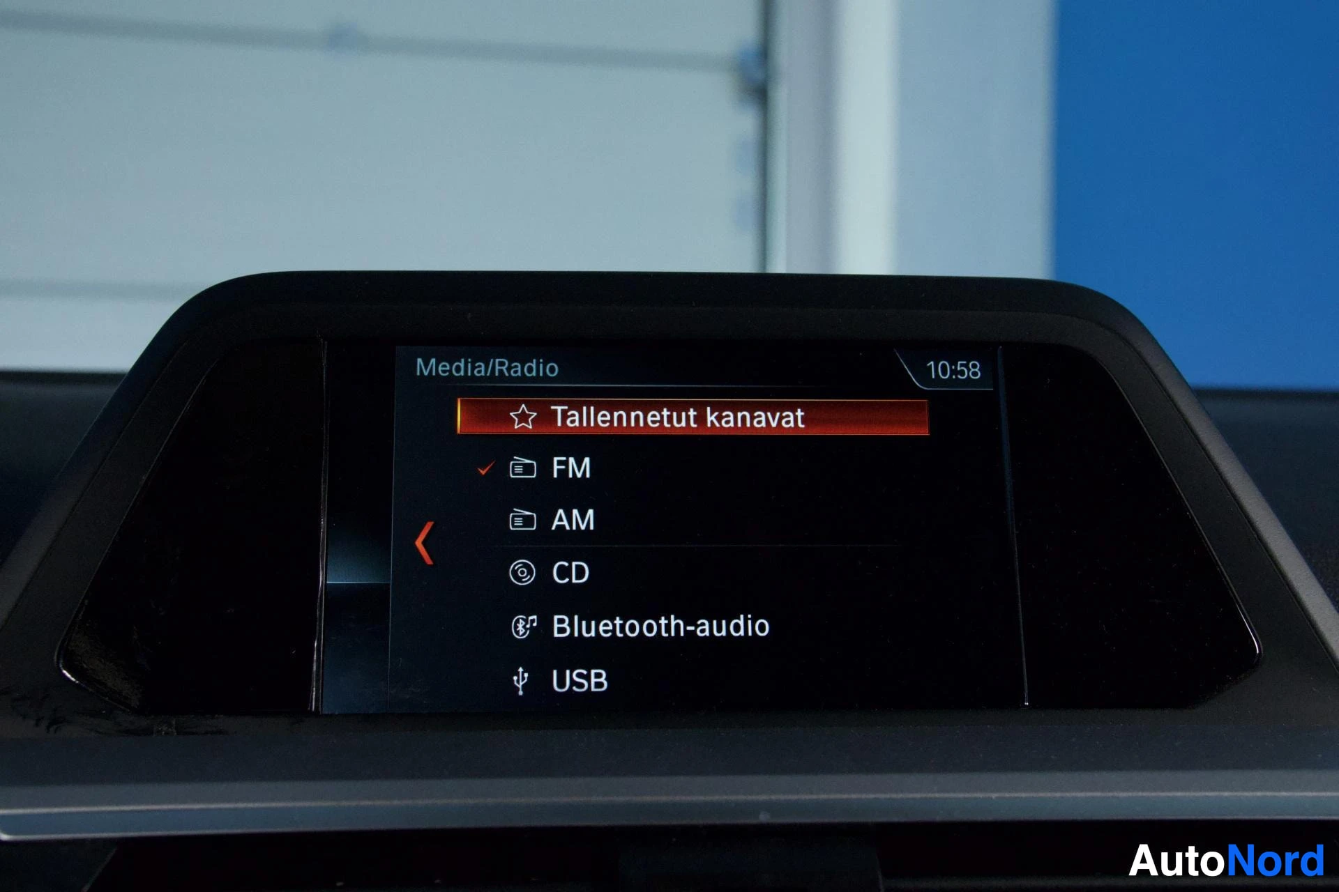 Yksityiskohta: Auton multimediajärjestelmän näyttö, jossa näkyy Media/Radio-valikko klo 10:53. Näytöllä on listattu valinnat: Tallennetut kanavat (FM valittu), AM, CD ja Bluet