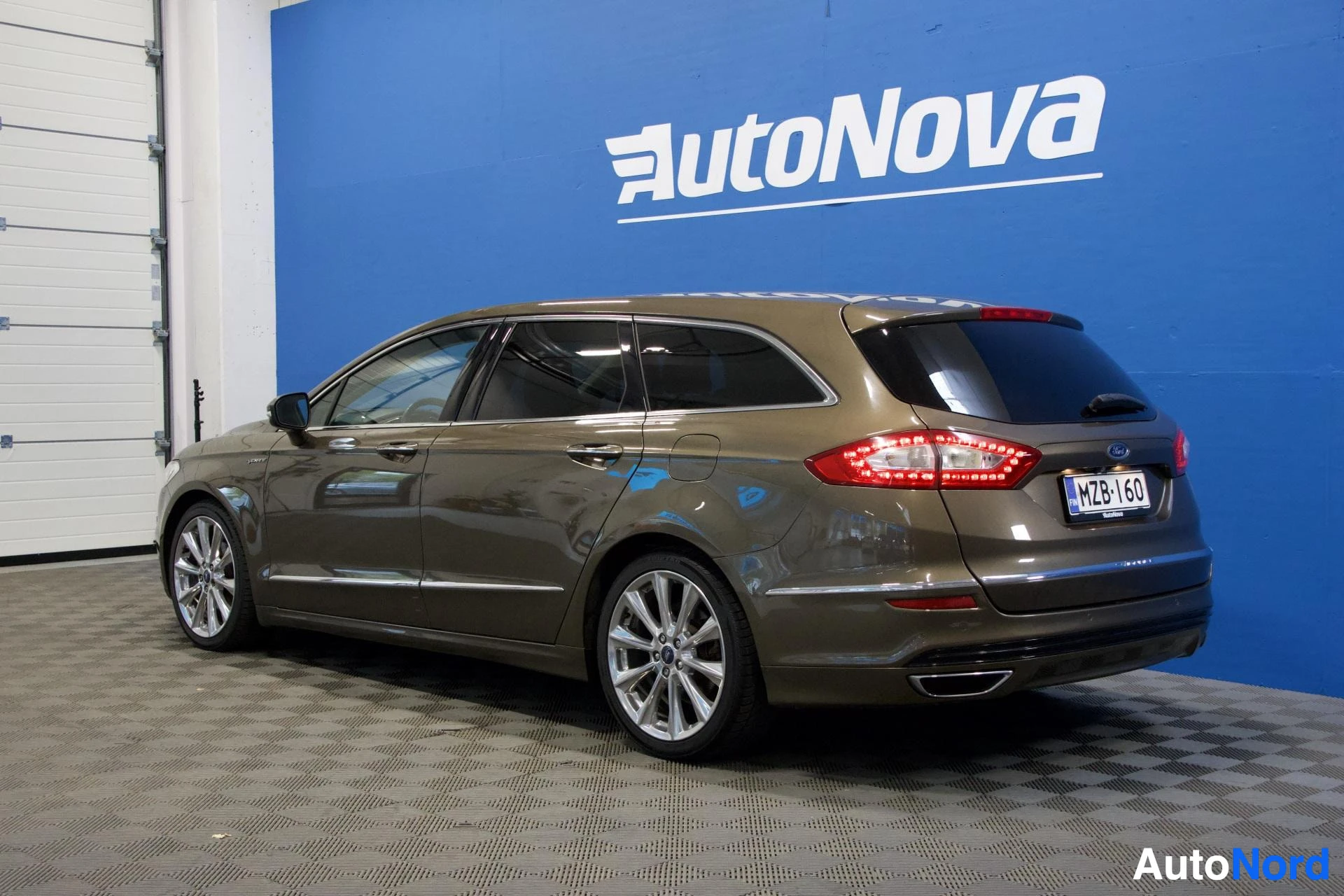 Takaviisto: Ford Mondeo -farmari takaa ja sivulta, väriltään ruskeansävyinen, sinisellä taustalla.