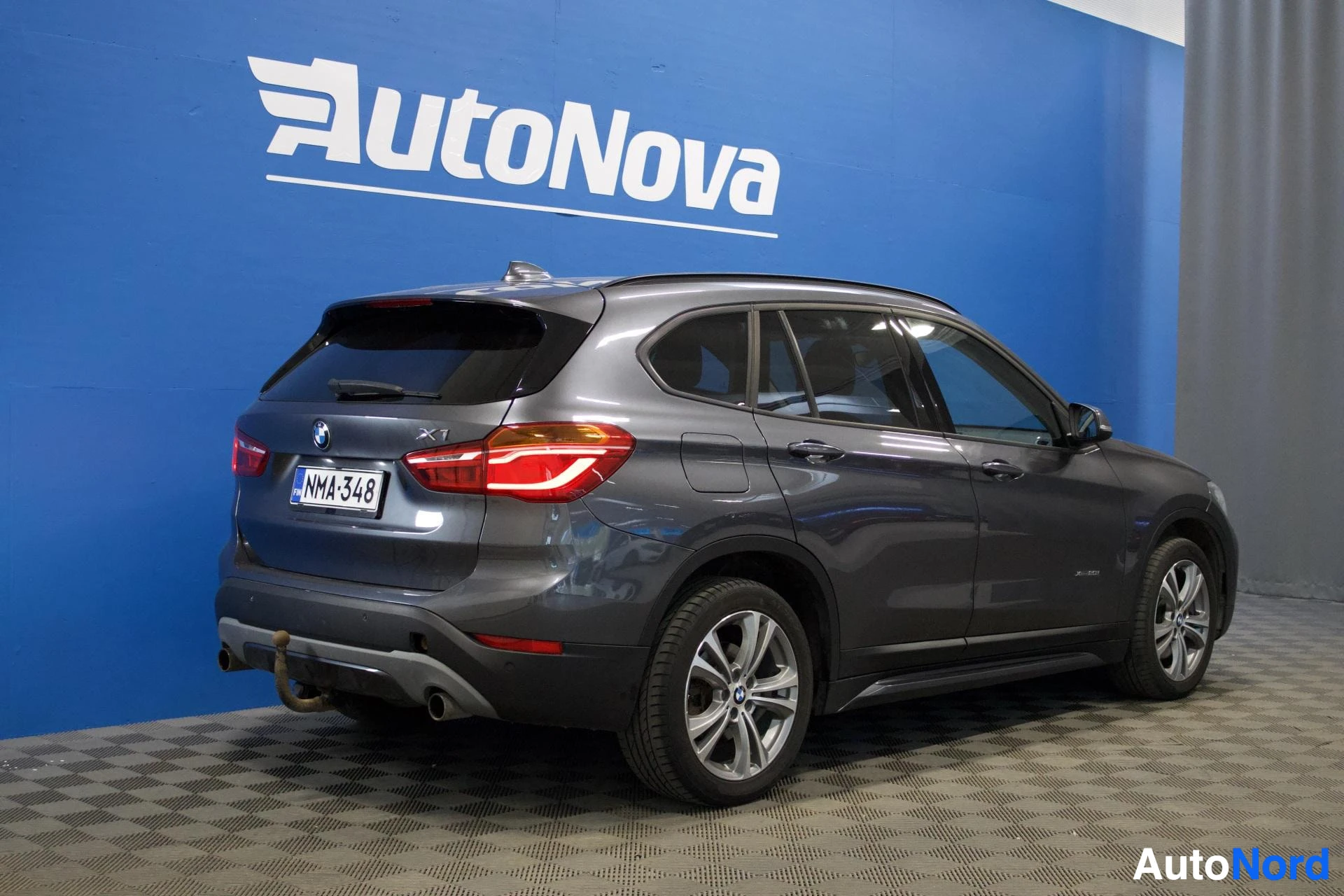 Takaviisto: BMW X1 -auton takaosan kolmeneljäsosakuva oikealta puolelta, autossa on vetokoukku ja rekisterikilpi ''.