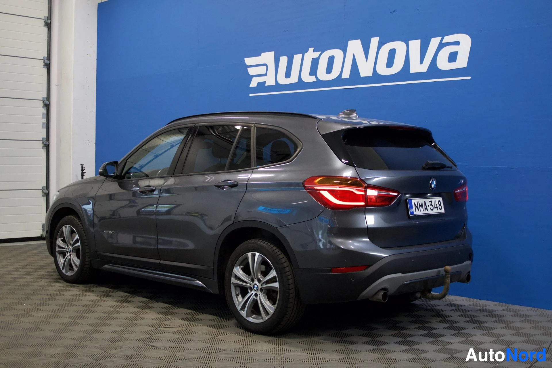 Takaviisto: BMW X1 -auton takaosan kolmeneljäsosakuva oikealta puolelta. Auto on harmaa ja siinä on vetokoukku.