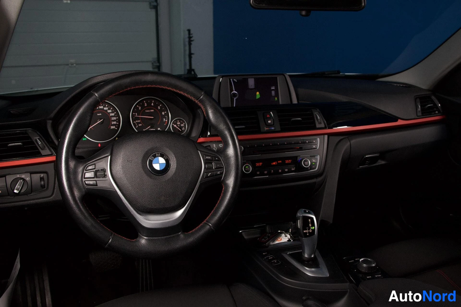 Ohjaamo: Kuljettajan näkökulma sisäpuolelta: mustan nahkaisen ratin, BMW-logon, kiihtyvyysmittarin, nopeusmittarin, pienemmän vasemman mittarin, punaisen sisustuskoriste