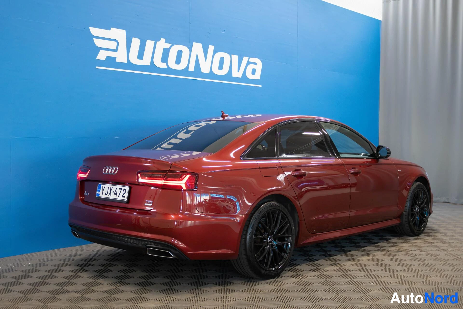 Takaviisto: Punainen sedan Audi A6:n taka-kolmasosakuva, jossa näkyvät takavalot, pakoputki ja rekisterikilpi. Autossa on mustat vanteet.