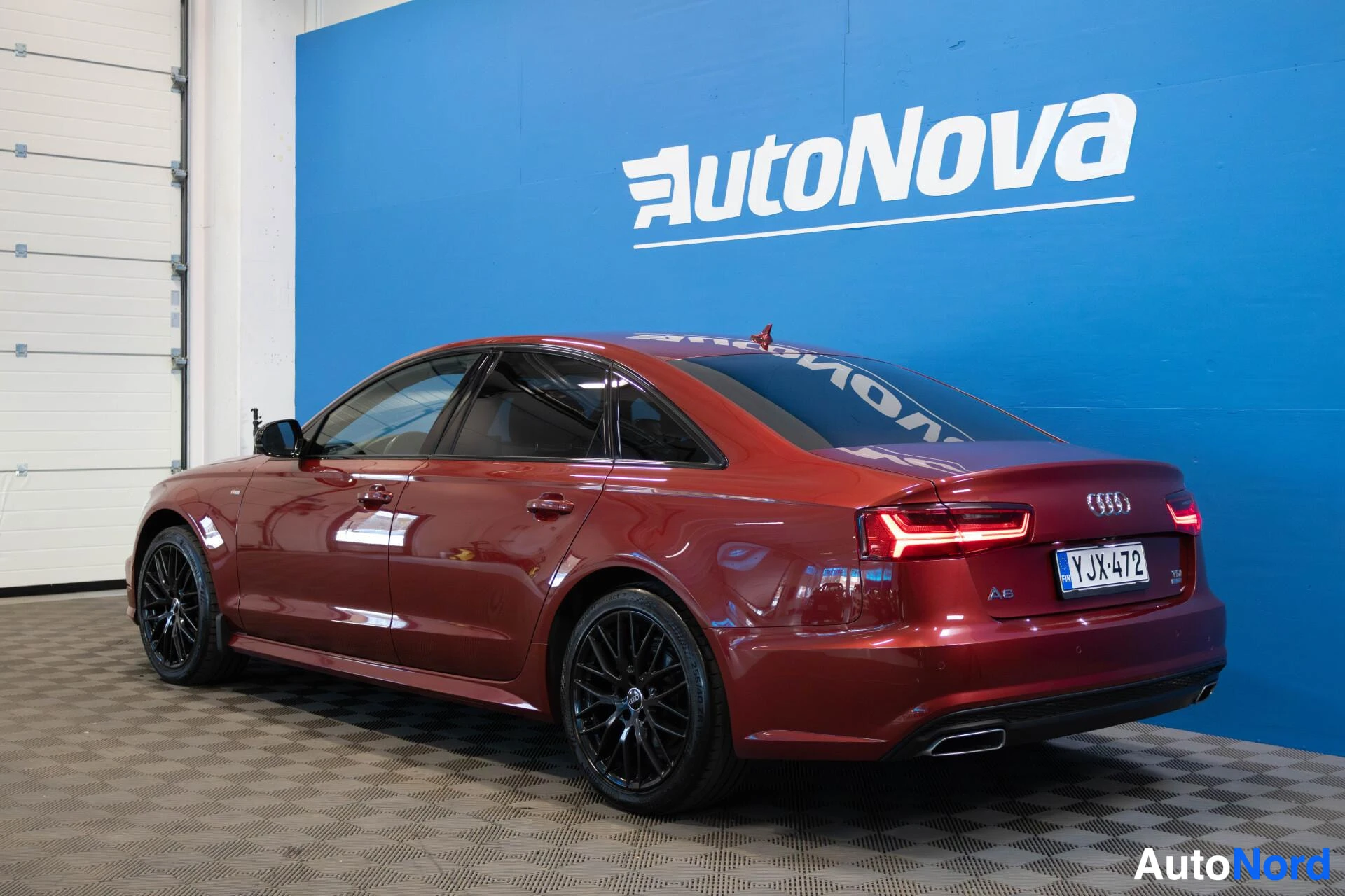 Takaviisto: Punainen sedan Audi A6:n taka-kolmasosakuva, jossa näkyvät takavalot, pakoputki ja rekisterikilpi. Autossa on mustat vanteet.