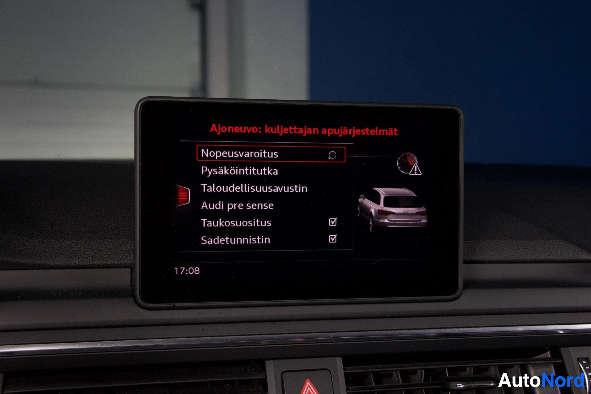 Yksityiskohta: Autoon asennetun näytön Ajoeuvo-päävalikko punaisen otsikon kanssa, näkyvät vaihtoehdot Nopeusvaroitus, Pysäköintitutka, Taloudellissuussavustin, Audi pre sense