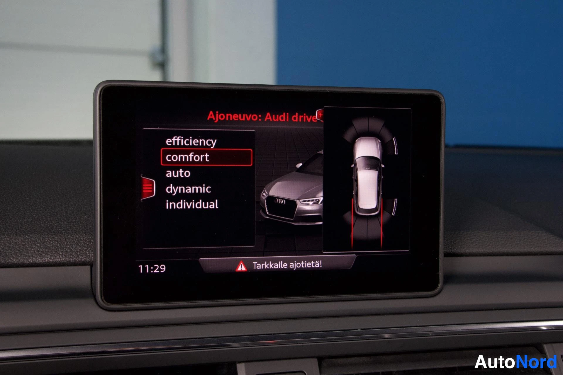 Yksityiskohta: Infotainment-näyttö Audi drive select -valikolla, jossa näkyy ajoneuvon ylhäältä kuvattu näkymä. Näytön alaosassa varoitus Tarkkaille ajotieta.