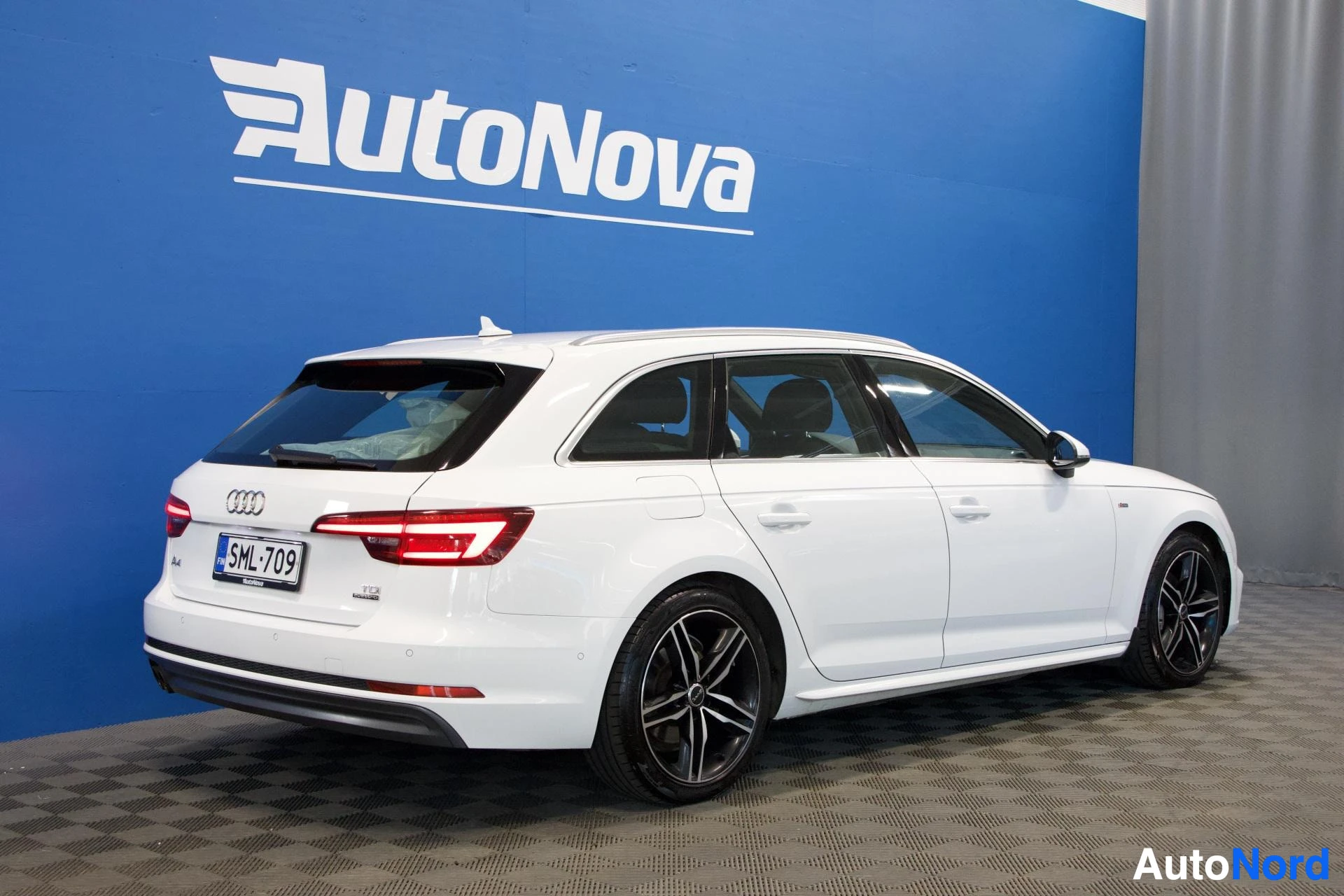 Takaa: Valkoinen Audi A4 Avant takaosasta, rekisterikilpi näkyvissä, sininen AutoNova-tausta