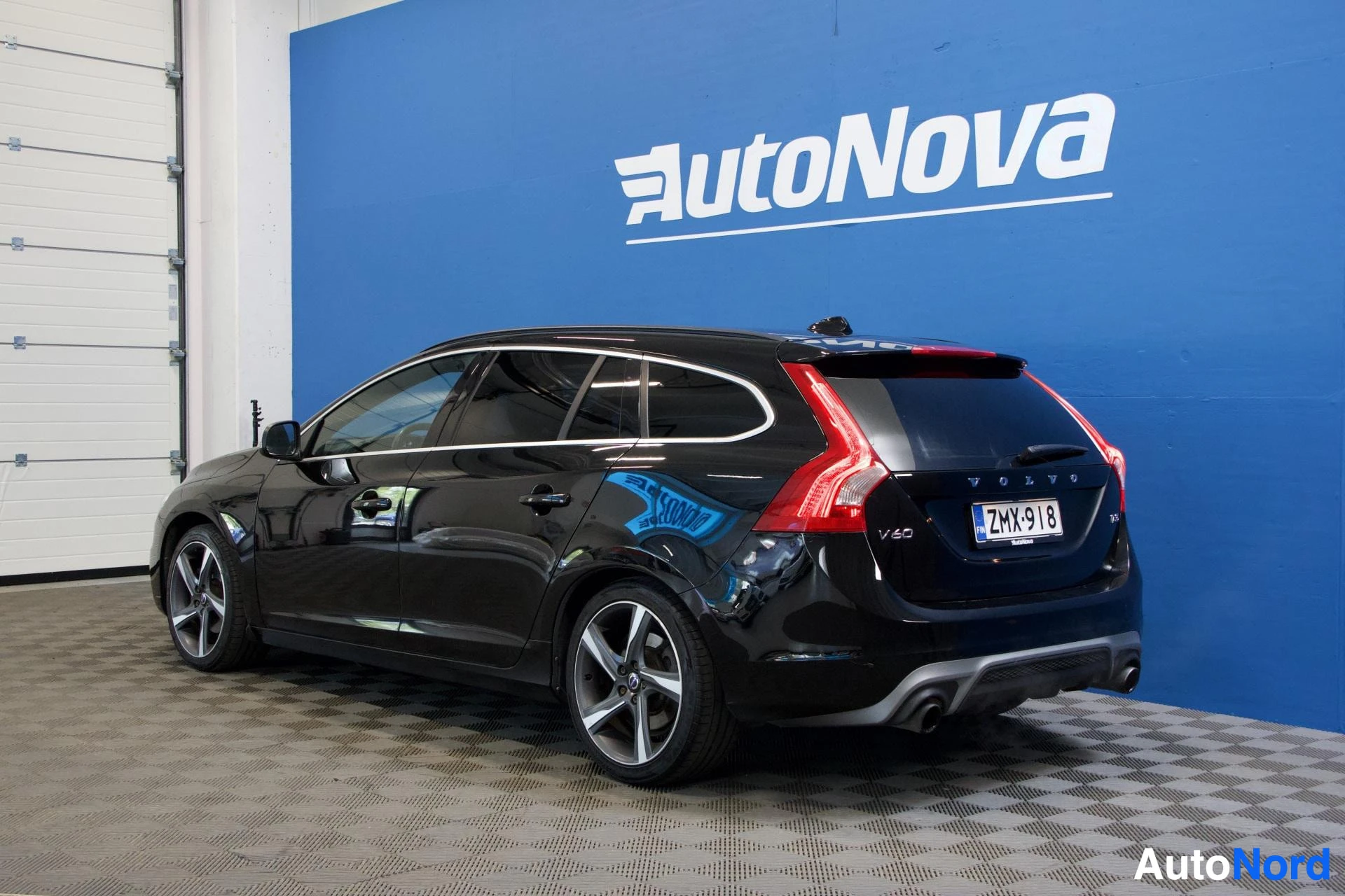 Etuviisto, nokka vasemmalle: Musta Volvo V60 kolmen neljänneksen kulmasta vasemmalta edestä, näkyvissä etu- ja vasen sivu, oikea ovi auki, rekisterikilpi ZM-918, valkoiset vanteet