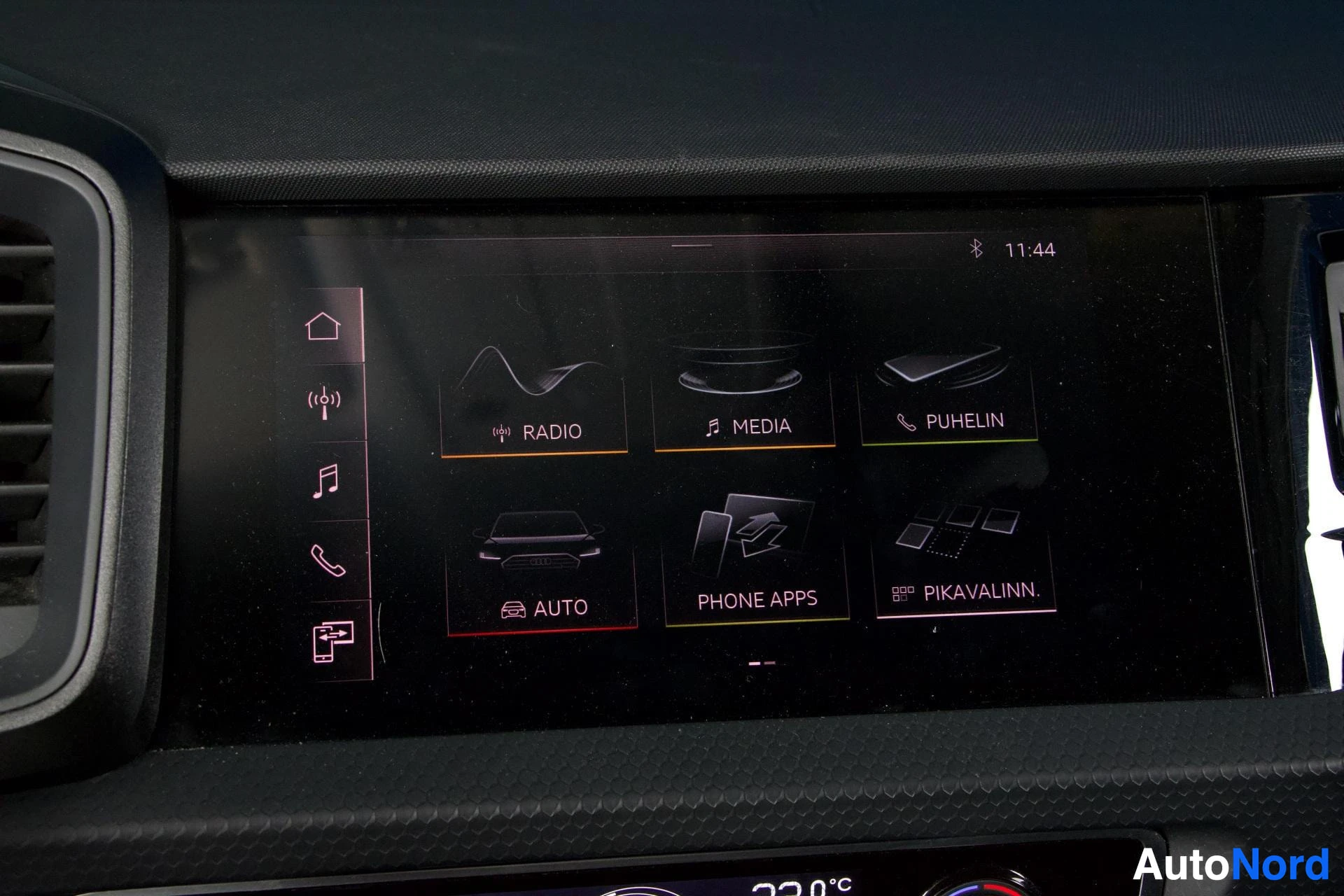 Yksityiskohta: Keski-infotainment-näyttö; valikkokuvakkeet näyttävät RADIO, MEDIA, PUHELIN, AUTO, PHONE APPS ja PIKAVALINN. tekstit.