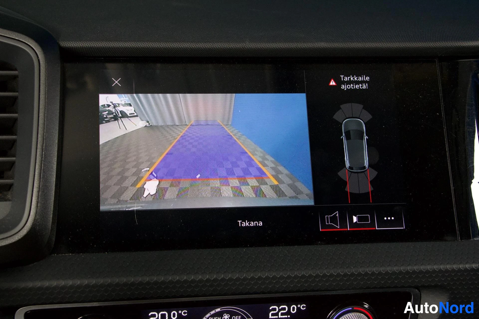 Yksityiskohta: Infotainment-näytön takana-kamera -näkymä, jossa näkyy violetti parkkeerausalue ja ajoneuvon ylhäältä näkymä oikealla puolella.
