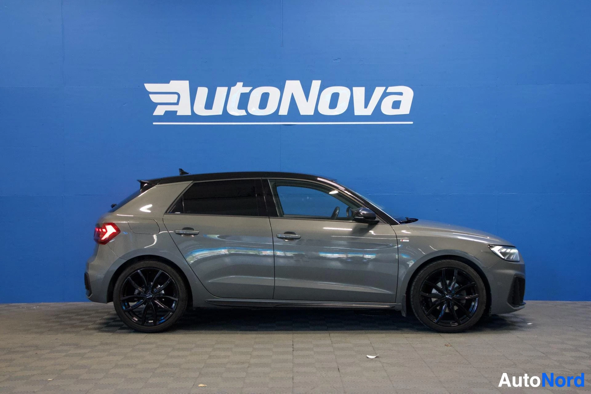 Sivulta: Audi A1 Sportback harmaa, koko auto näkyy sivusta vasemmalta, tummat vanteet, sininen tausta