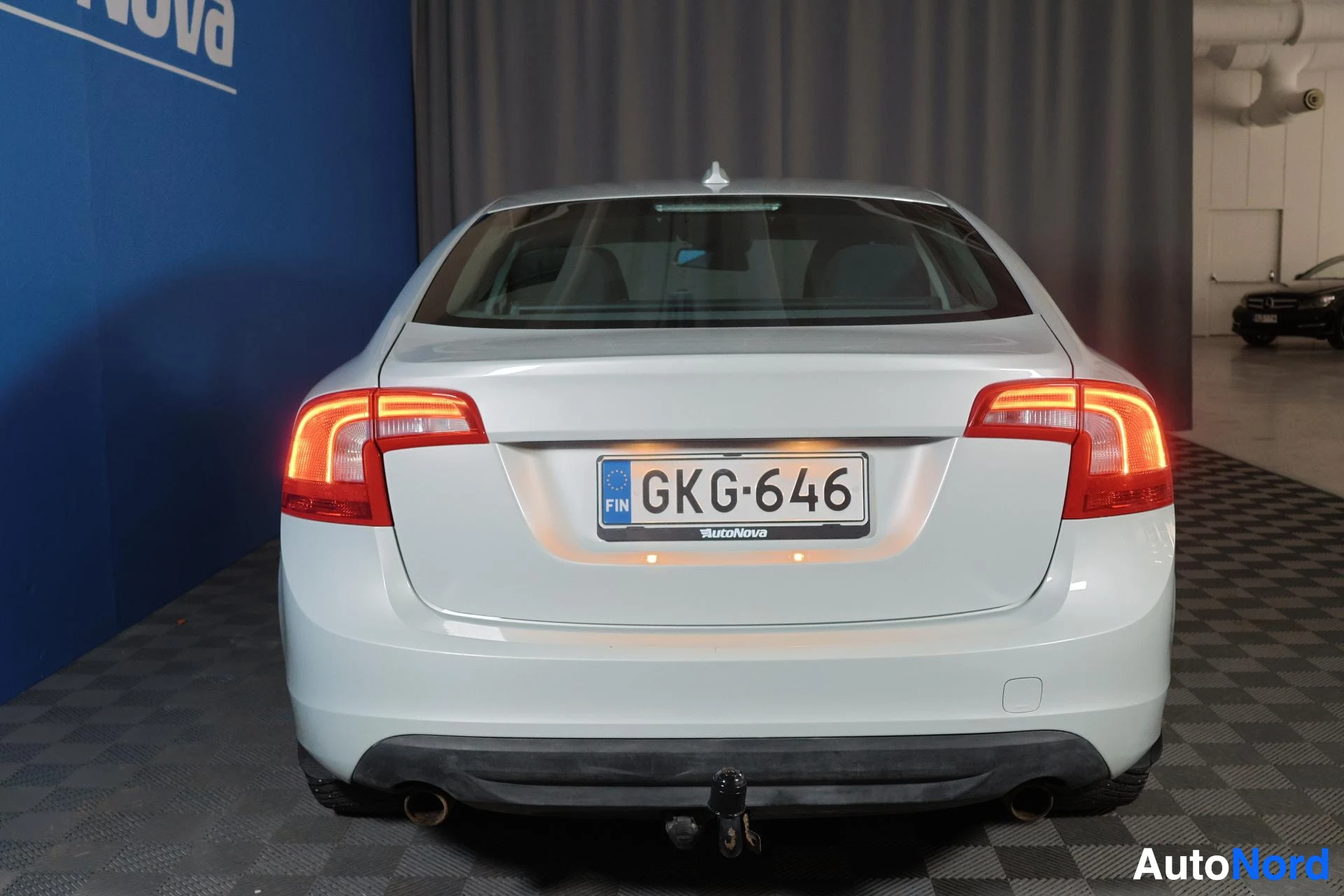 Takaa: Volvo S60 takaa kuvattu, rekisteritunnus näkyvillä, takavalot syttyneenä punaisina, vetokoukku näkyvissä auton alla, alumiiniset navakuvut