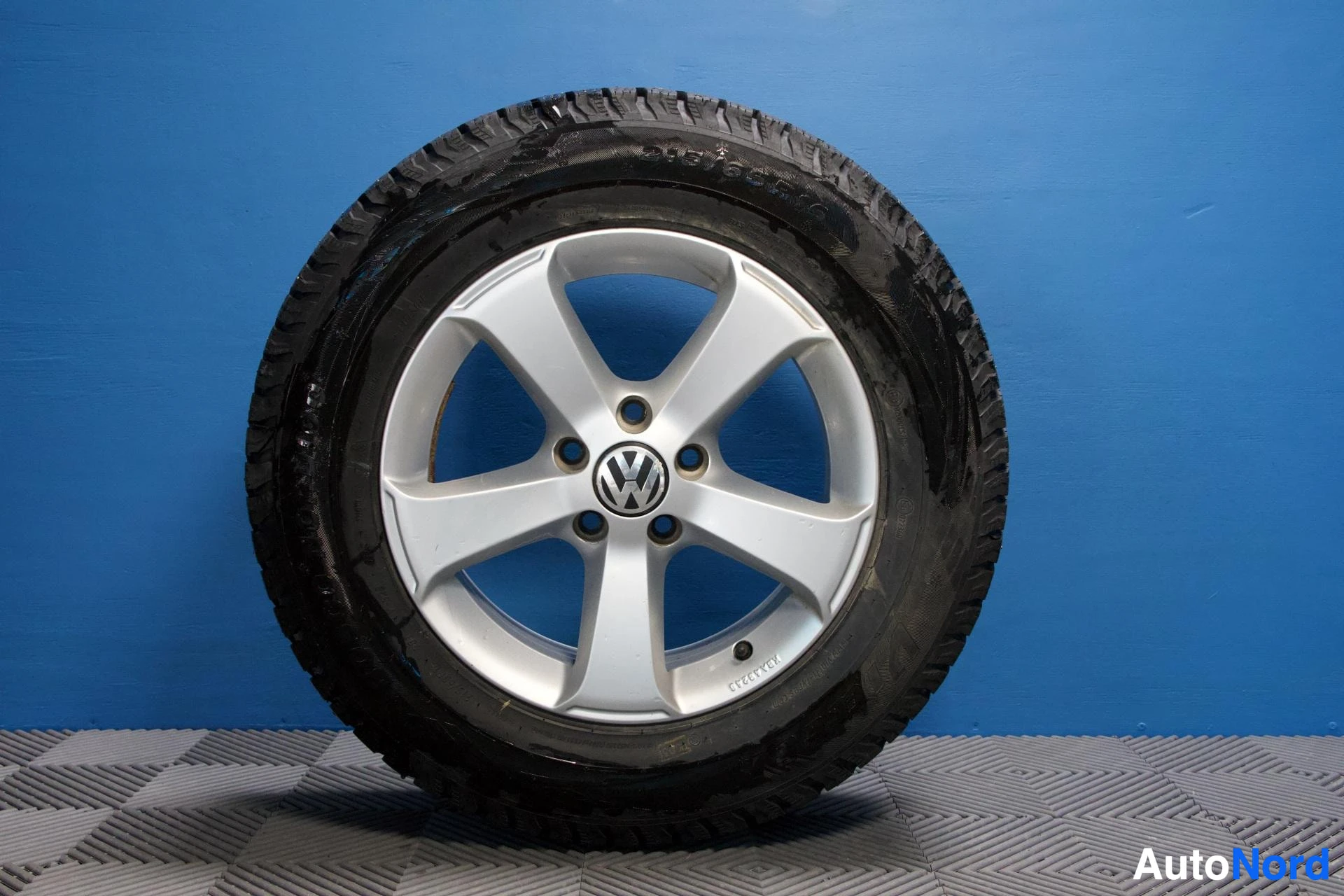 Yksityiskohta: Yksittäinen kevytmetallivanne, jossa on talvirengas. Vanteen keskellä on Volkswagenin logo.