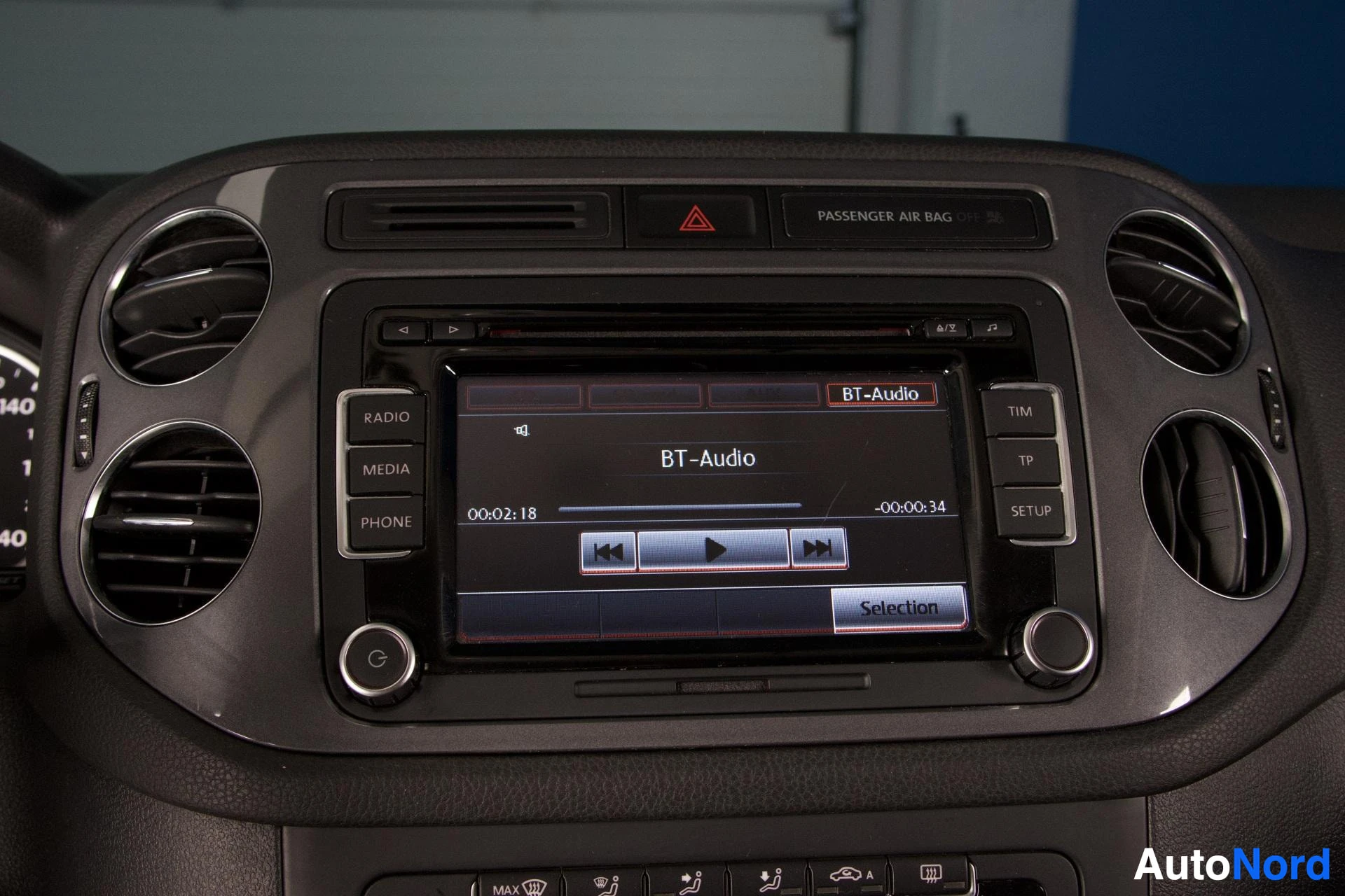 Ohjaamo: Kuva auton infotainment-järjestelmän näytöstä, joka näyttää Bluetooth-audion toistokuvan. Näytöllä on toistopainikkeet ja tieto "BT-Audio". Ilmastoinnin suulakk