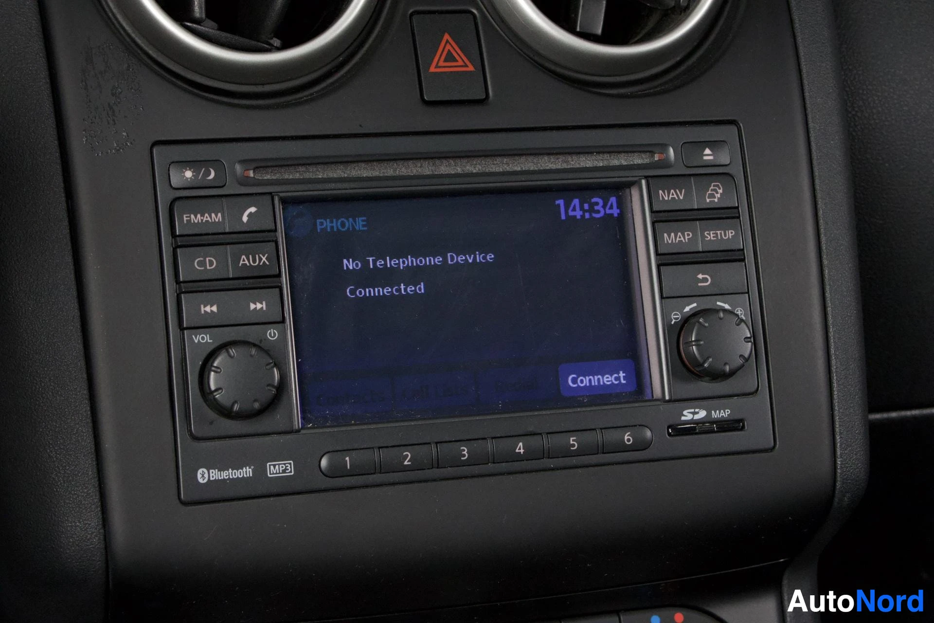 Yksityiskohta: Autoradio ja navigaatiolaite mustalla paneelilla, näytöllä "No Telephone Device Connected" ja kello näyttää 14:34