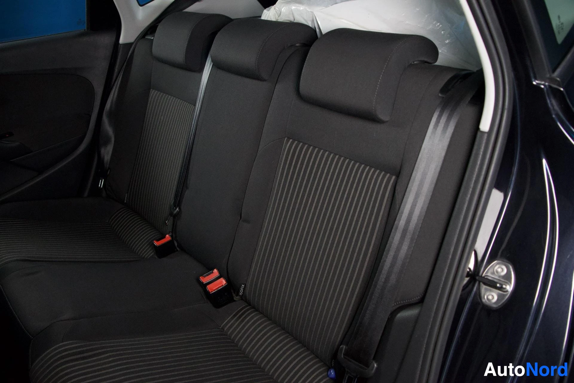 Takaistuimet: Takaistuimet. Istuimet ovat mustaa kangasta, jossa on ohuita vaaleita pystyraitoja. Kaksi ISOFIX-kiinnityspistettä näkyvissä.