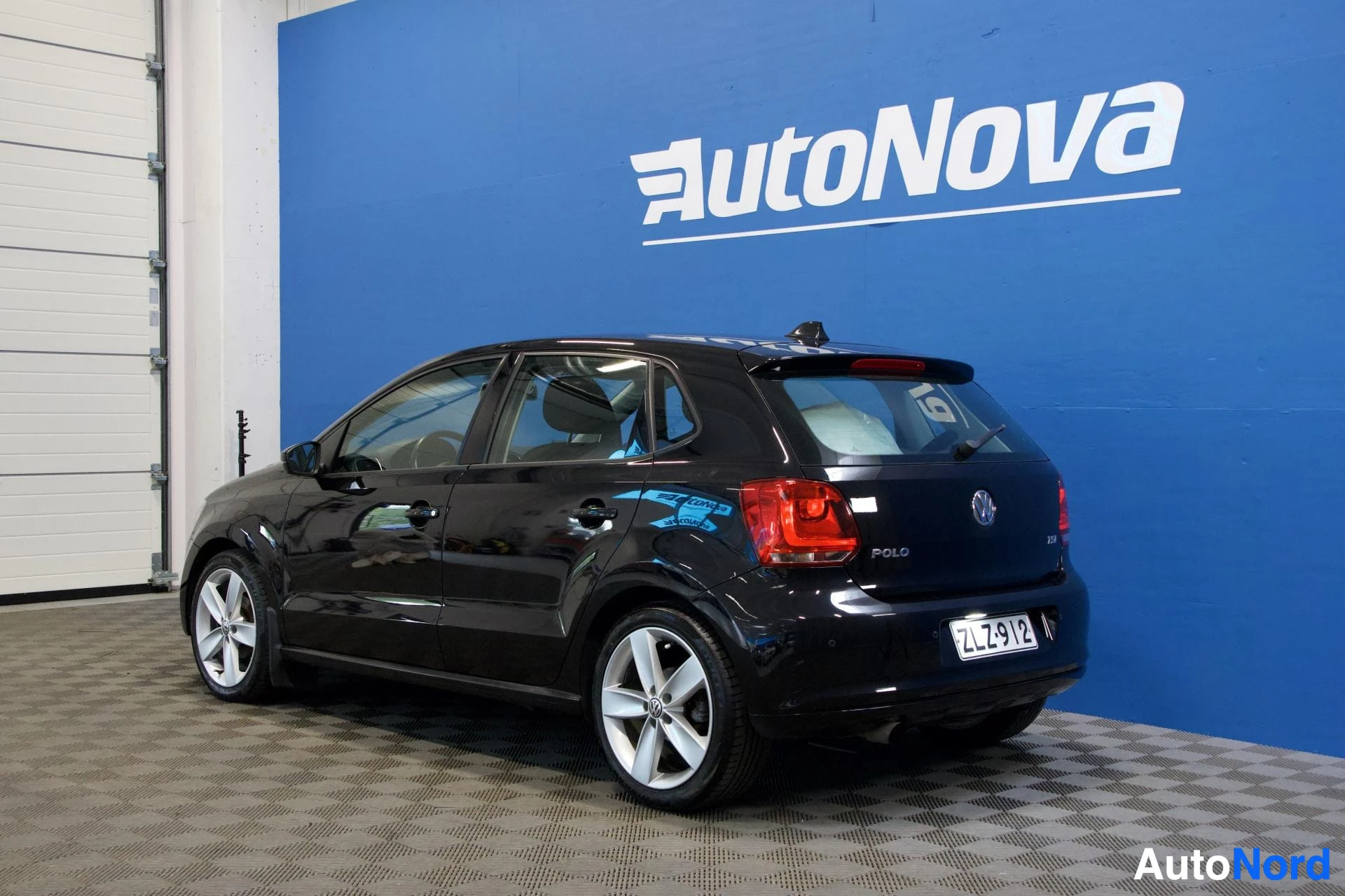 Takaviisto: Musta viisiovinen hatchback-auto, jossa on alumiinivanteet, on kuvattu takaviistosta vasemmalta puolelta autonäyttelytilassa. Auton takaluukussa on rekisterikil