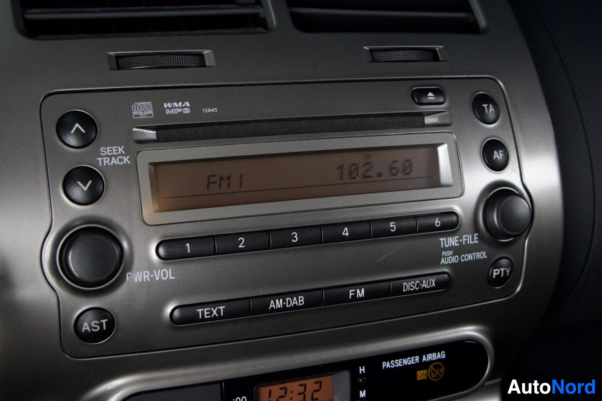 Yksityiskohta: Lähikuva auton keskikonsolin äänentoistoyksiköstä, jossa näkyy FM-radiotaajuus 102.60 ja WMA/MP3-yhteensopivuuden merkintä.