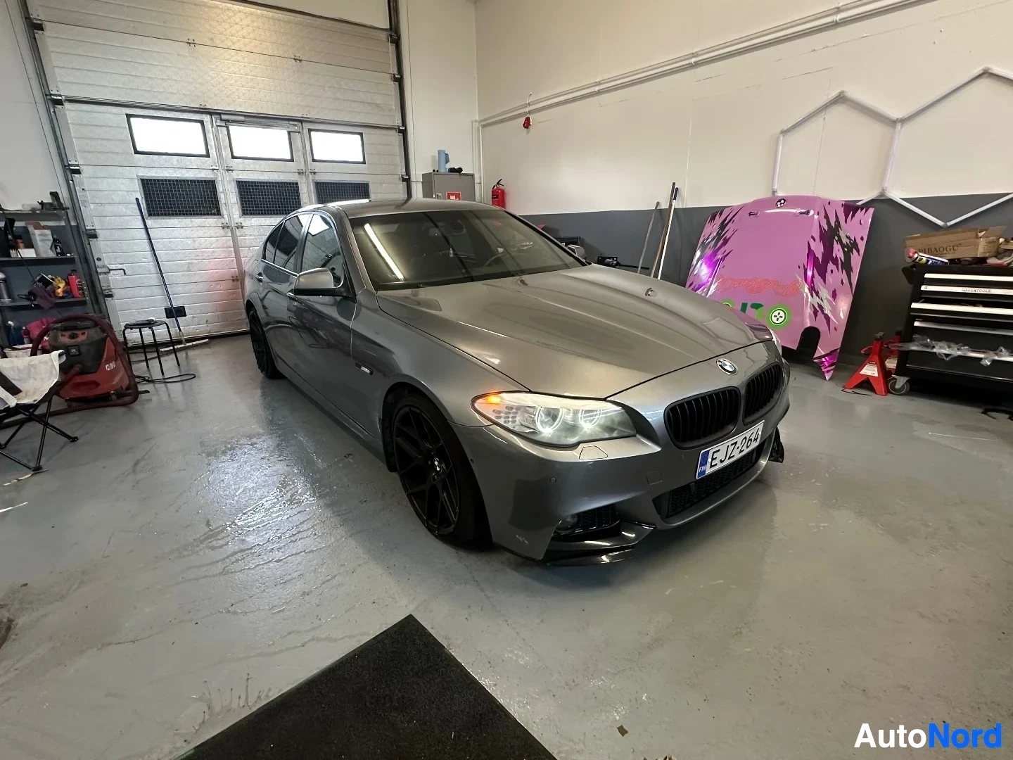 Etuviisto, nokka oikealle: Hopeanvärinen BMW sedan, kuvattu vasemmalta sivulta hallissa. Rekisterikilvessä teksti LJ18JZF.