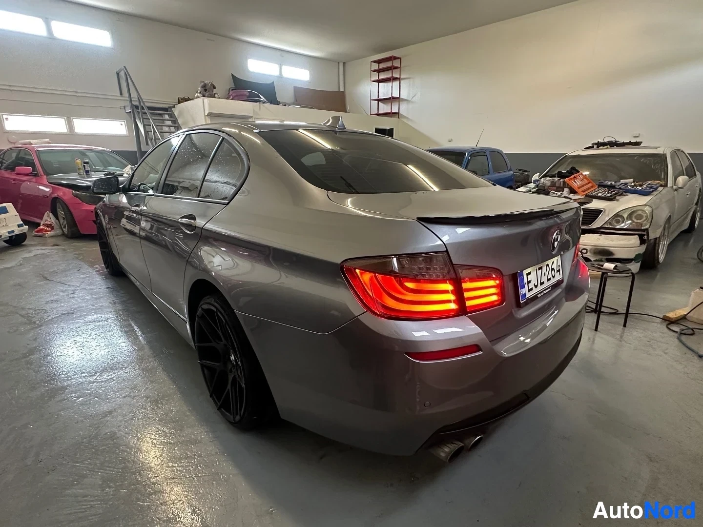 Takaa: Hopeanvärinen BMW sedan takaa hallissa, punaiset LED-takavalaisimet näkyvissä, rekisterikilvessä LJ18JZF.