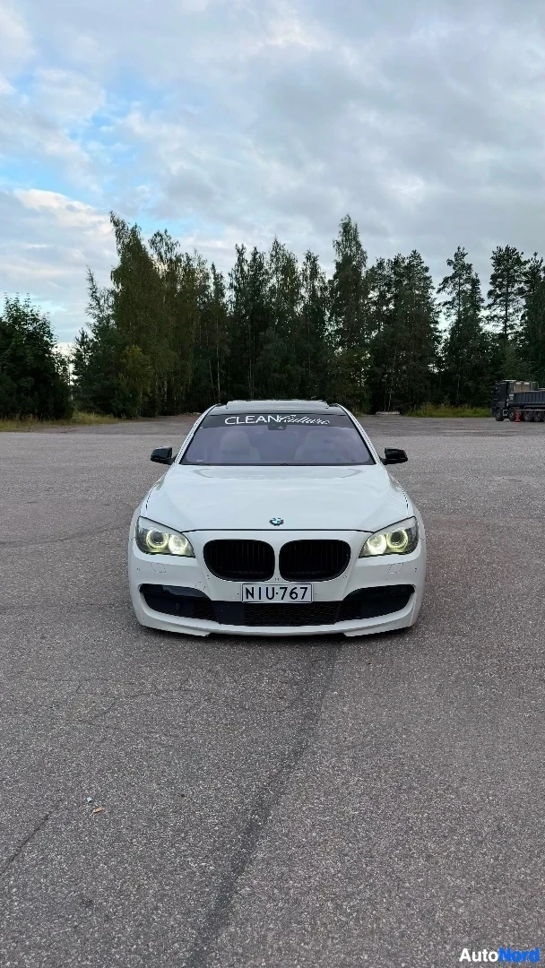 Edestä: Valkoinen BMW-sedan edestä, pysäköitynä asfalttialueelle. Etupuoli keskittäin. Rekisterikilpi näkyy: NIU 767. Tuulilasin yläosassa teksti CLEAN.