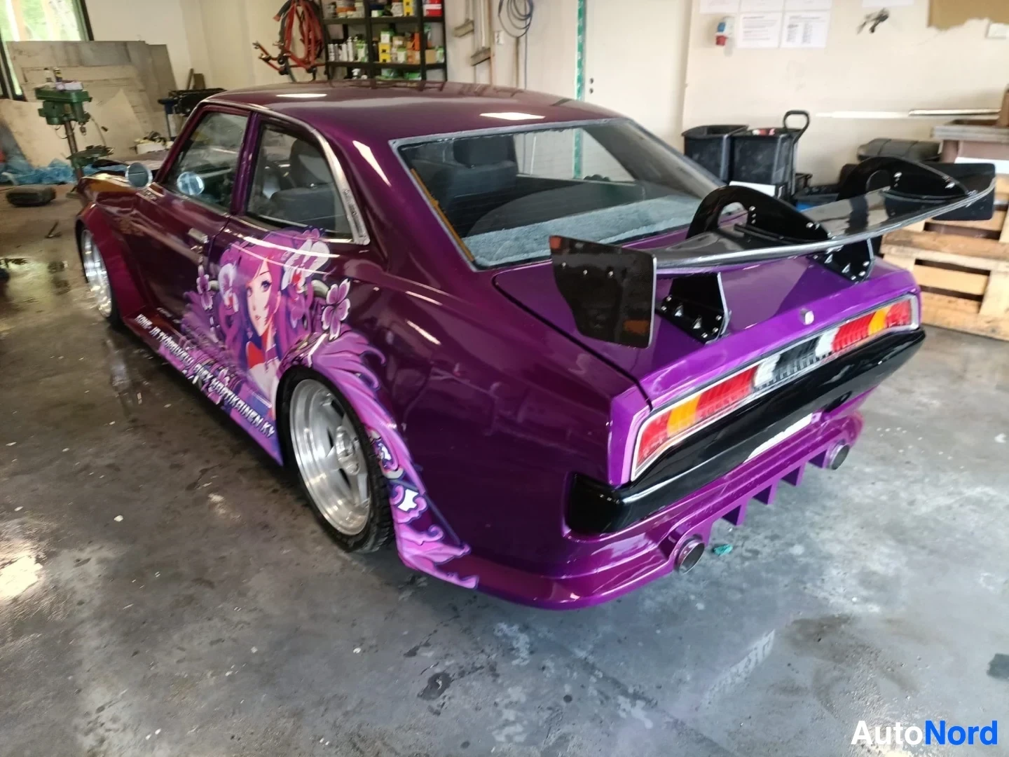 Takaviisto: Pinkki-violetti coupe taaksepäin hallissa, auki olevin verhoin, yksityiskohtainen takatasku-keulakeula mukaansa omaa käärittävää grafiikkaa.