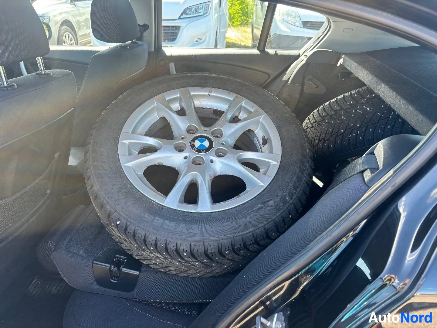 Tavaratila: Auton renkaat ja vanteet oviaukosta kuvattuna, näkyy suuri alloy-vanne BMW-logolla ja nastarenkaita