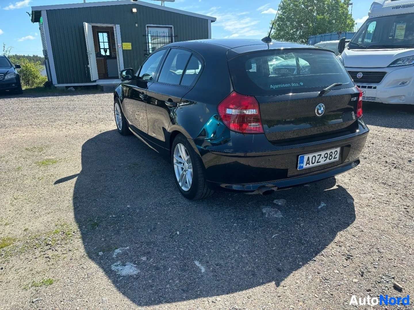 Takaviisto: Musta BMW 116i takaa ja sivulta kuvattuna kolmivinkelikulmassa, näkyvissä takaosa sekä osa sivusta.